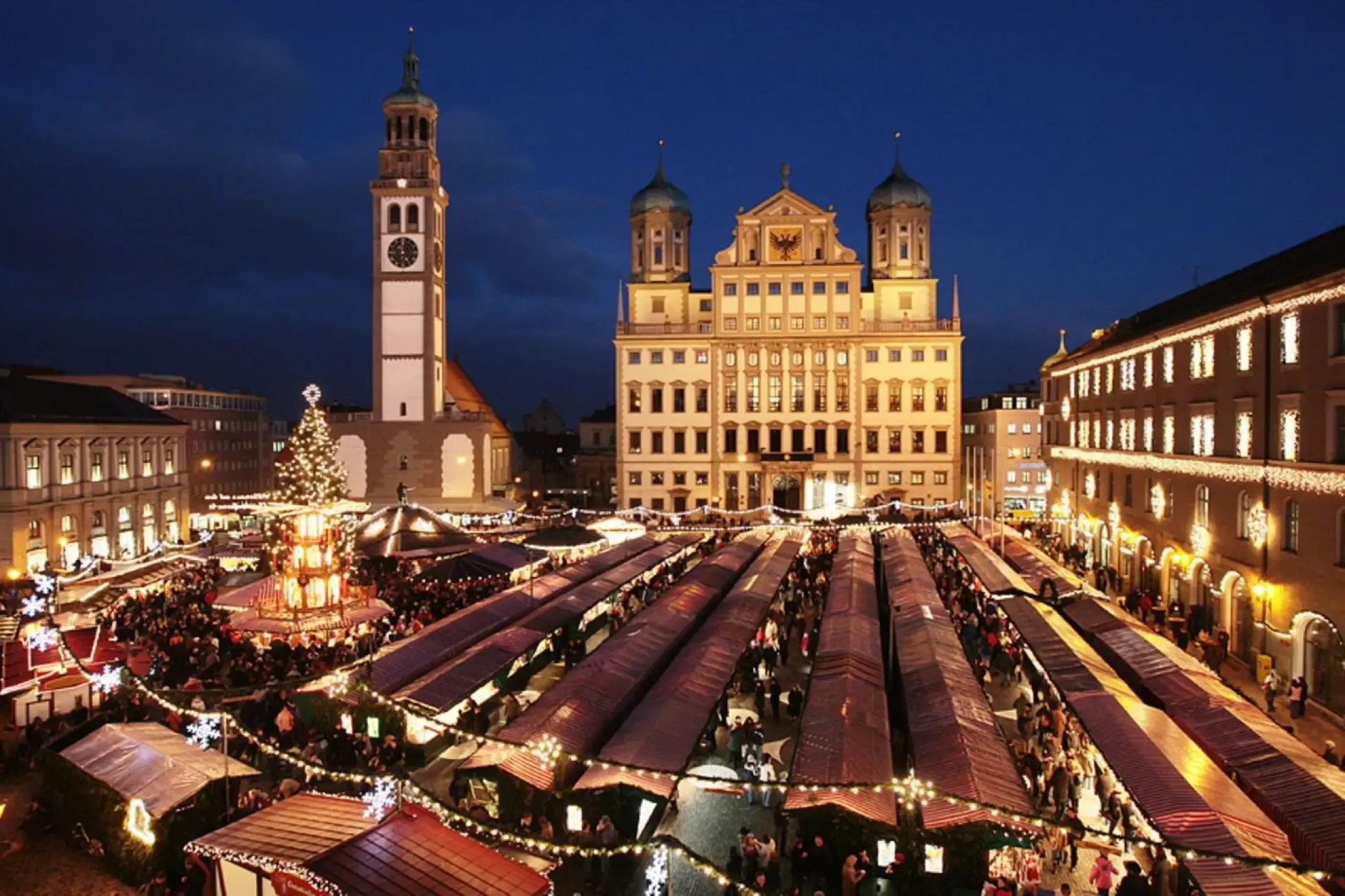 Augsburg Christmas market at night with historic town hall, clock tower, and illuminated stalls.
