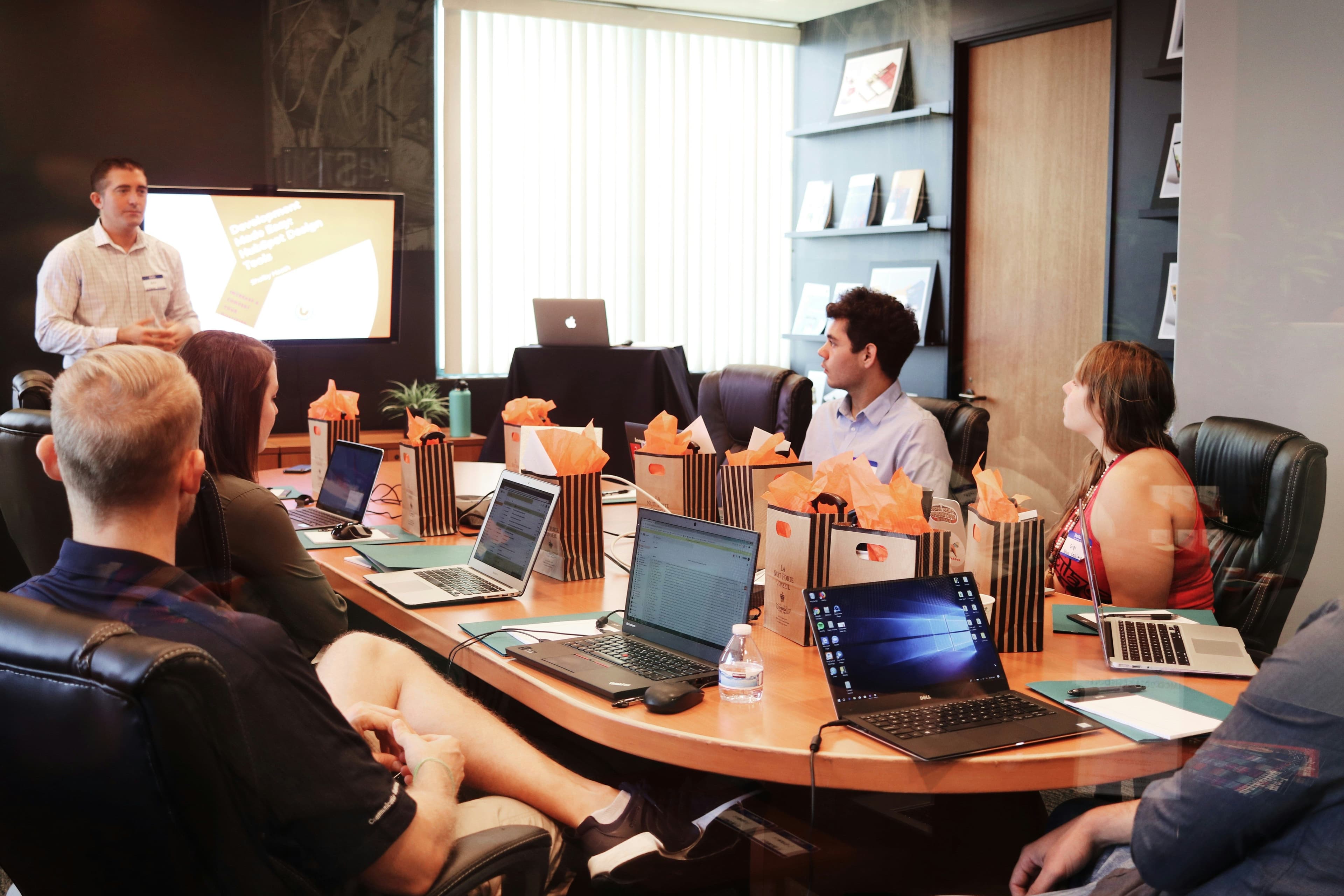 Attendees participate in a corporate workshop in a modern conference room with laptops and gift bags.