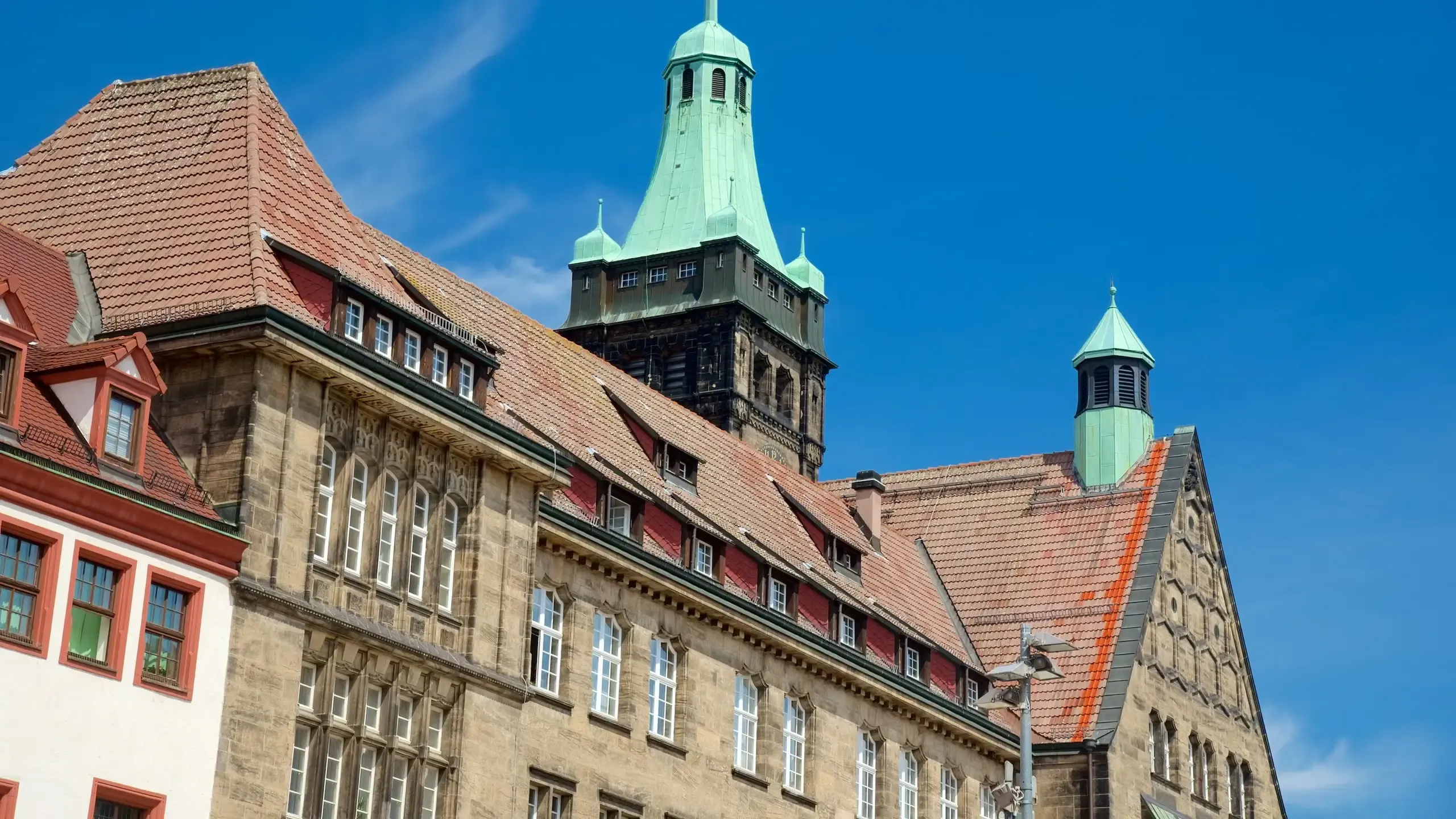 Historic stone building with terracotta roofs and green-domed towers under a blue sky in Chemnitz.