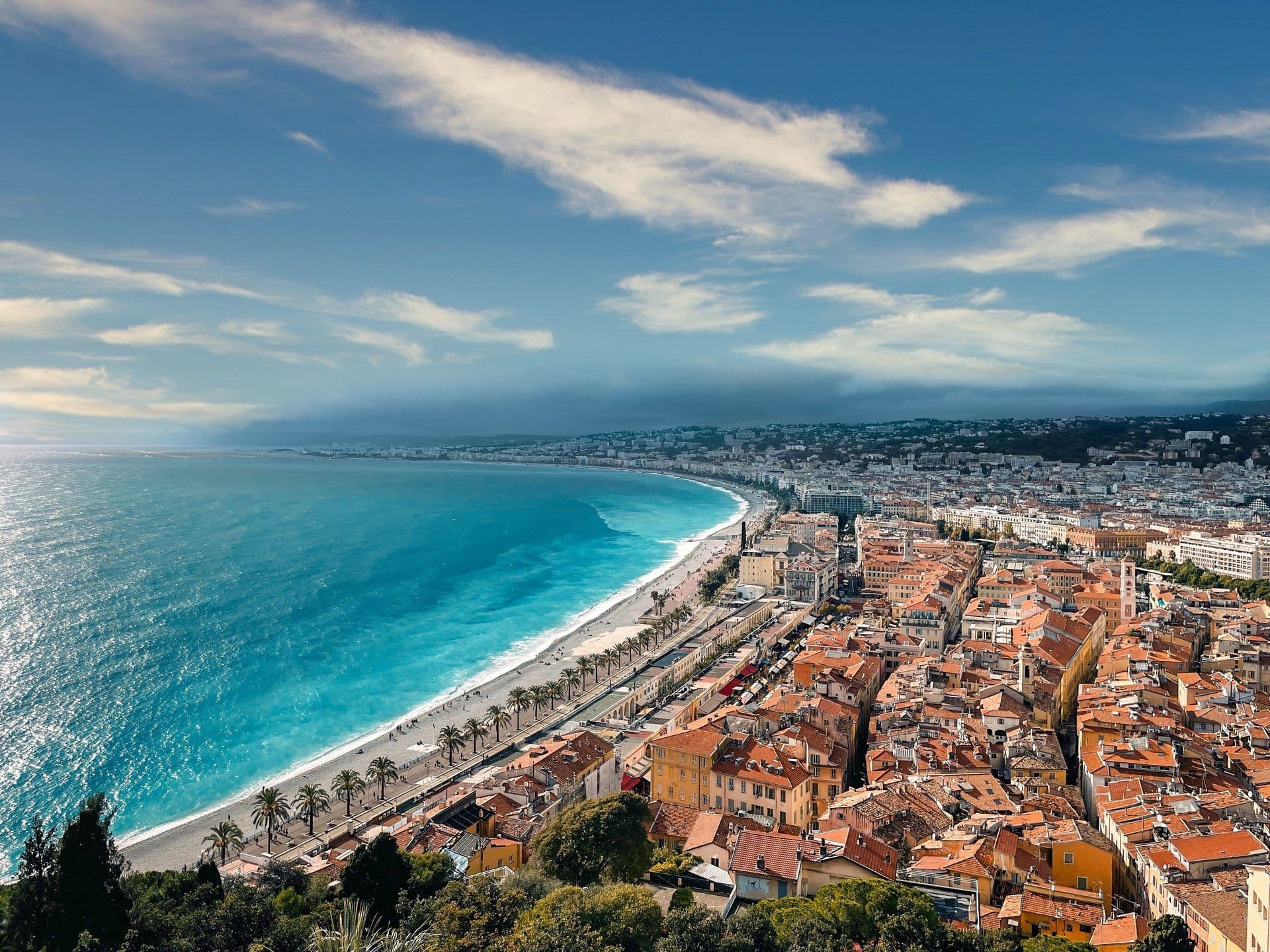 Aerial view of the turquoise Mediterranean Sea, pebble beach, and historic city of Nice, France.