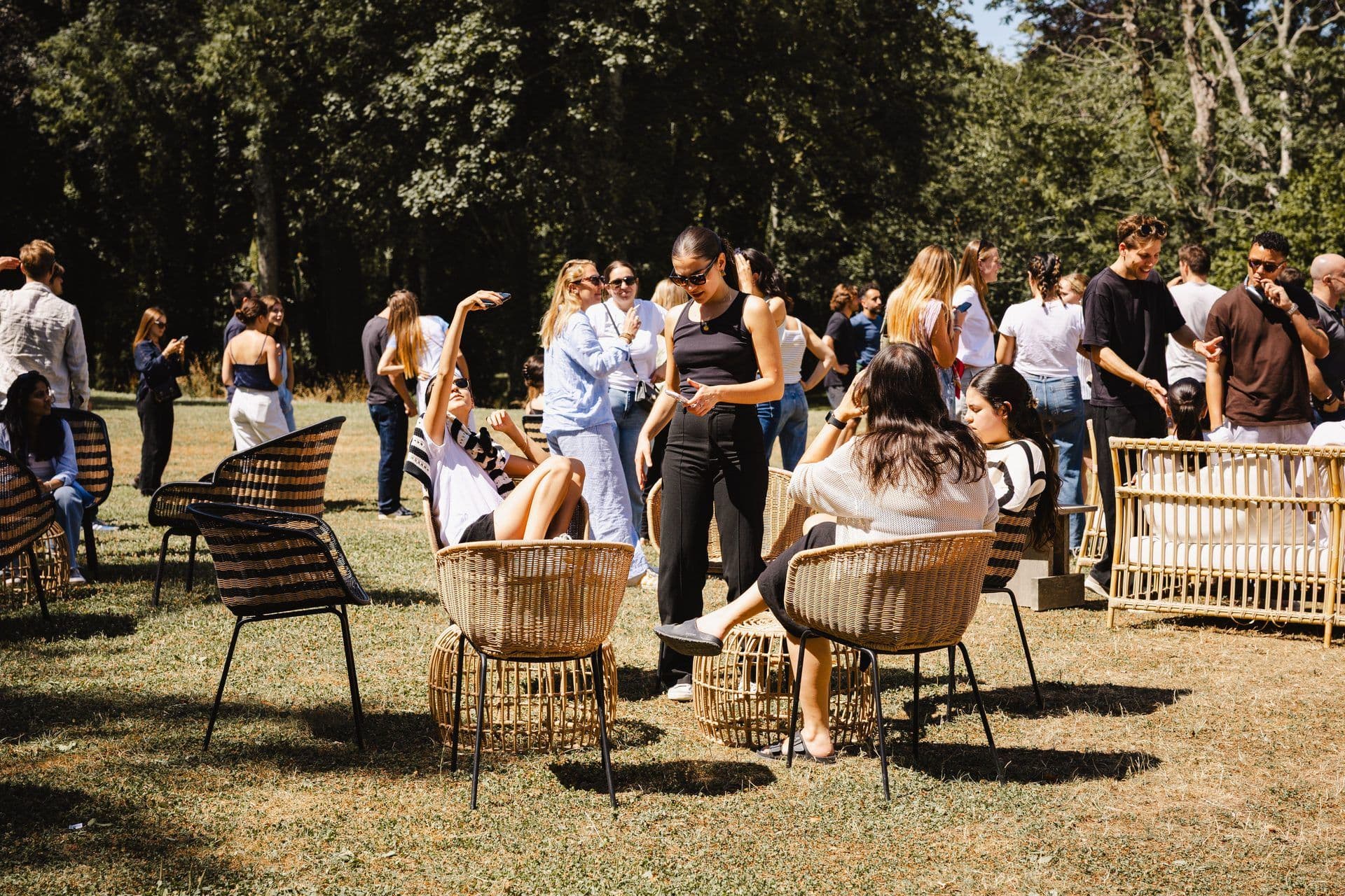 Attendees relax in wicker chairs and mingle on a sunny lawn during an outdoor corporate offsite.