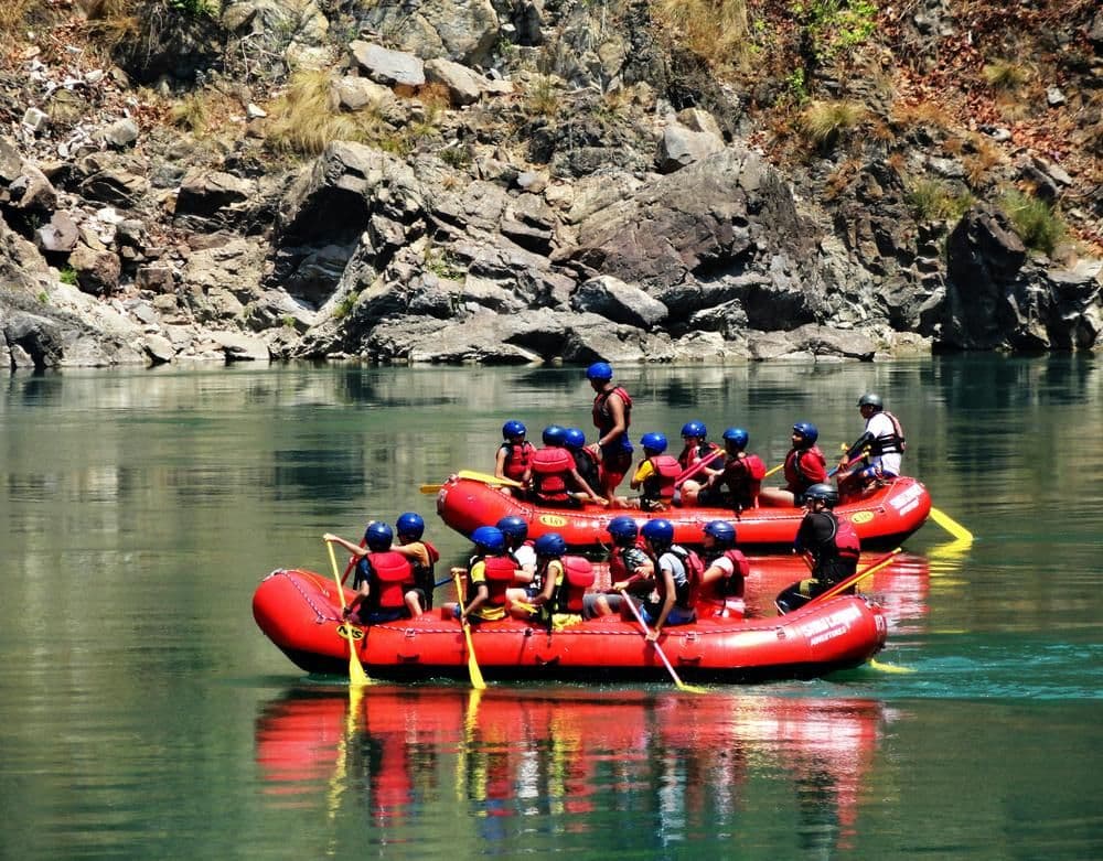 Corporate teams on red rafts with paddles and helmets engage in an outdoor team building activity on a calm
