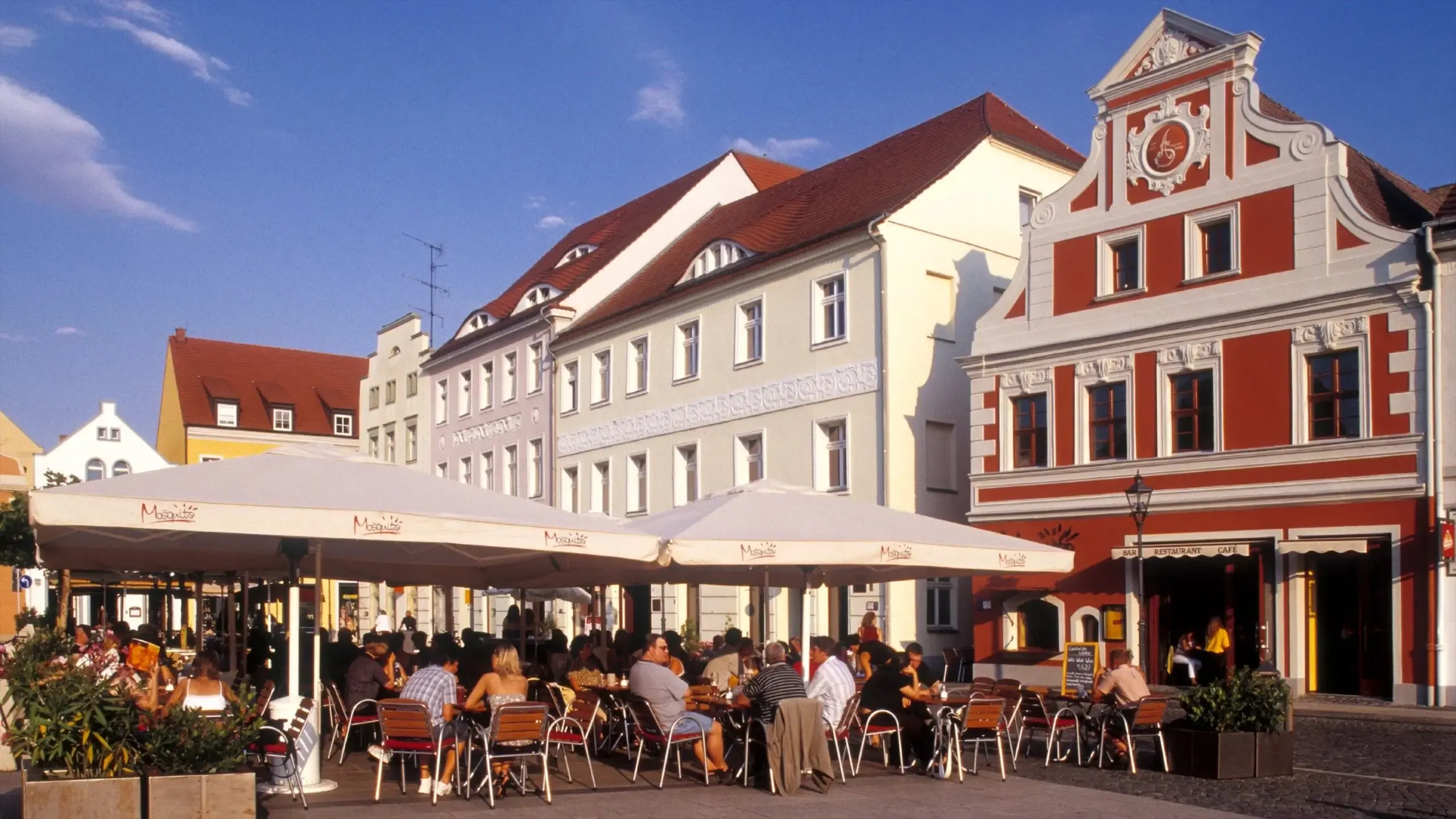 People enjoy a business lunch at an outdoor cafe with historic buildings in Cottbus, Germany.