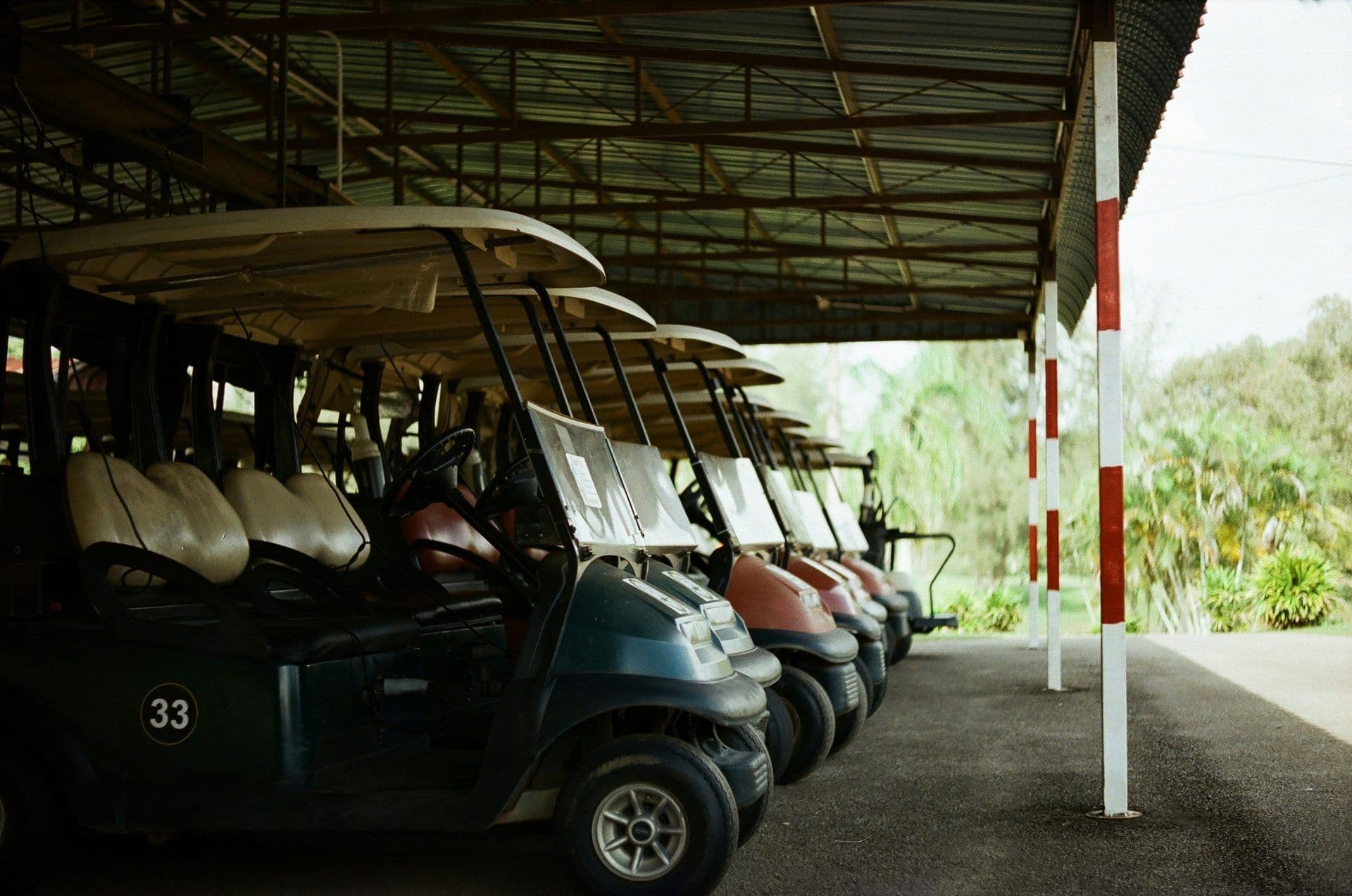 Row of golf carts parked under a metal roof, suggesting an outdoor corporate event or team offsite.