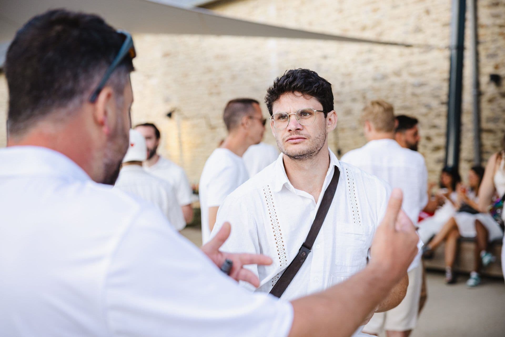 Two men converse during a corporate networking event at an outdoor venue with a stone wall.