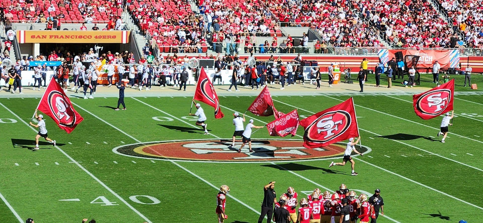 Flag bearers and players on the field of a San Francisco 49ers football stadium filled with spectators.