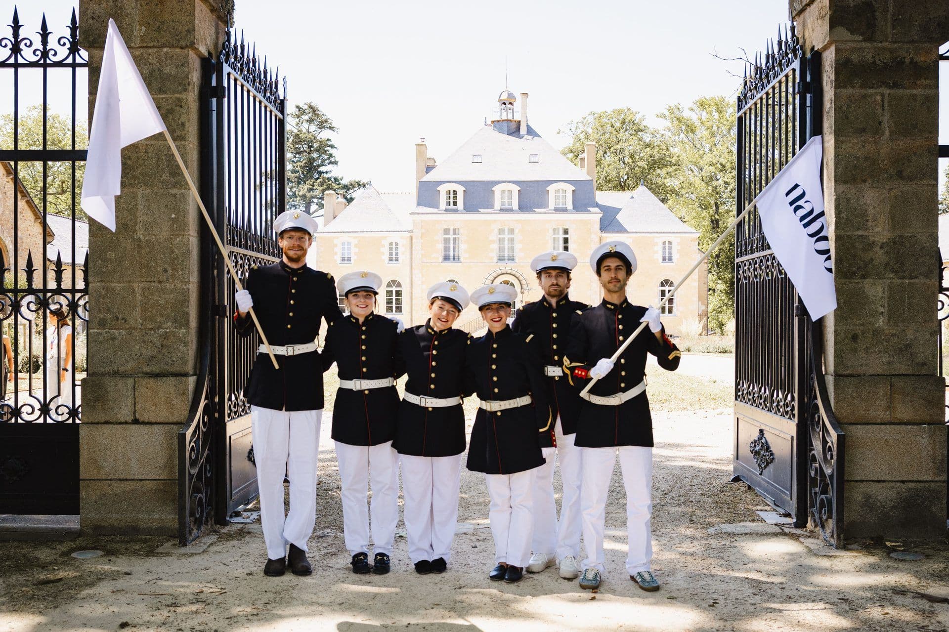 Six uniformed staff with flags welcome guests at a grand historic chateau, an ideal corporate event venue.