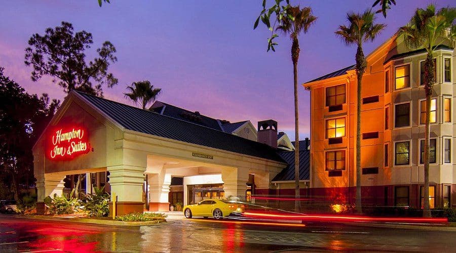 Hampton Inn & Suites hotel exterior at dusk with a glowing neon sign, palm trees