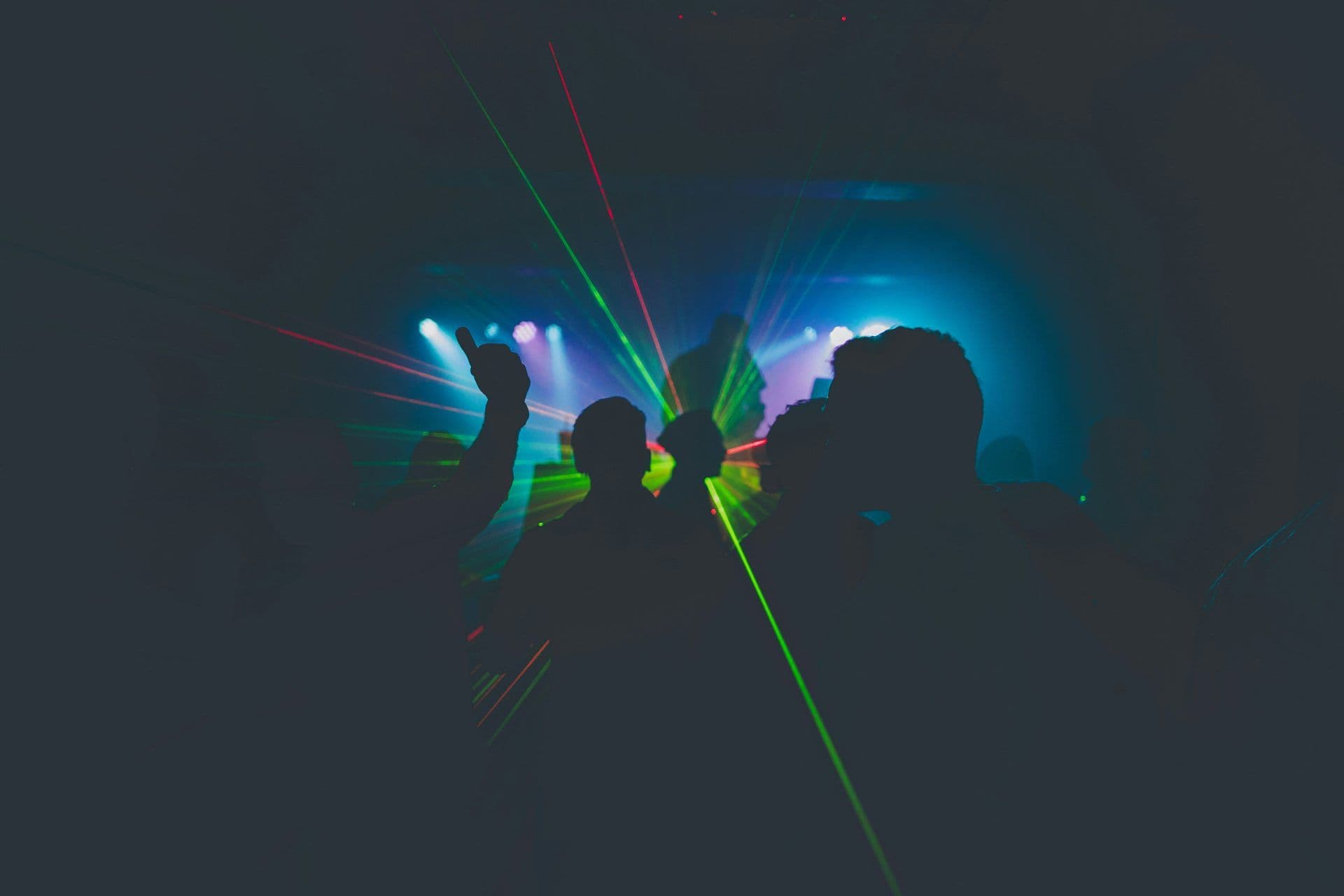 Silhouettes of people dancing under vibrant laser and stage lights at a corporate event.