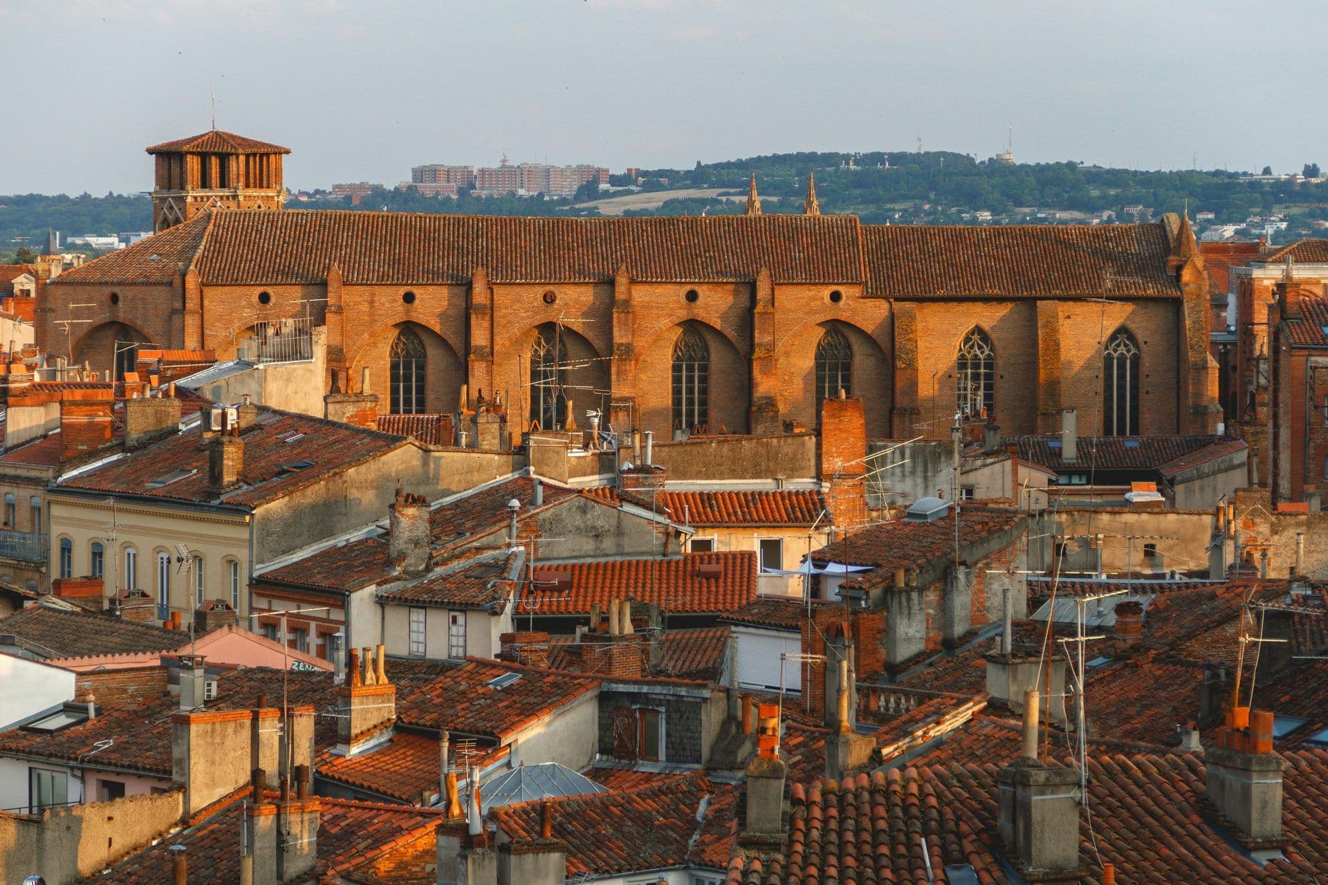 Toulouse, France cityscape with terracotta roofs and a large historic brick church at sunset.