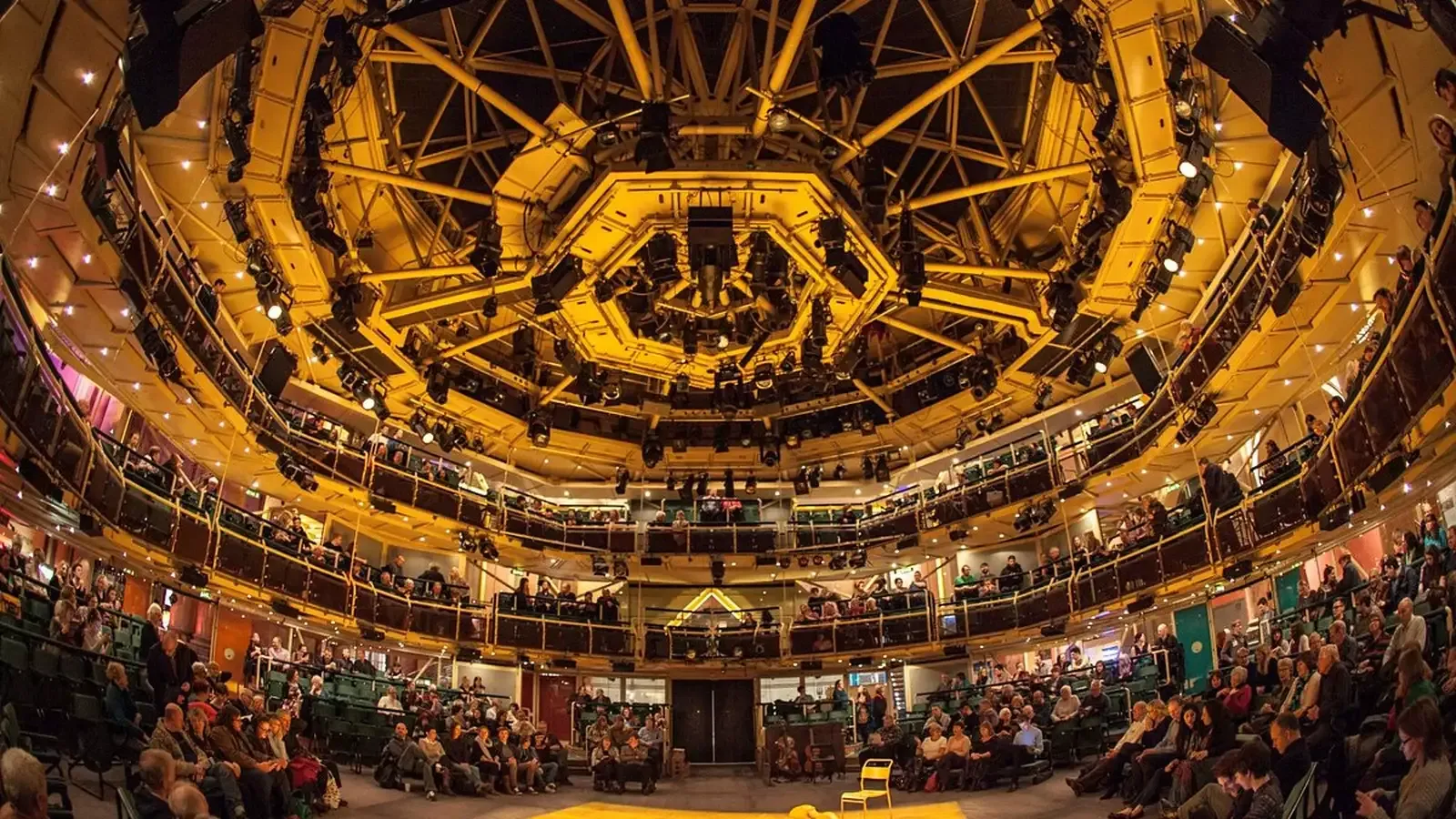 A large, multi-tiered auditorium with a complex lighting system, filled with attendees for a corporate event.