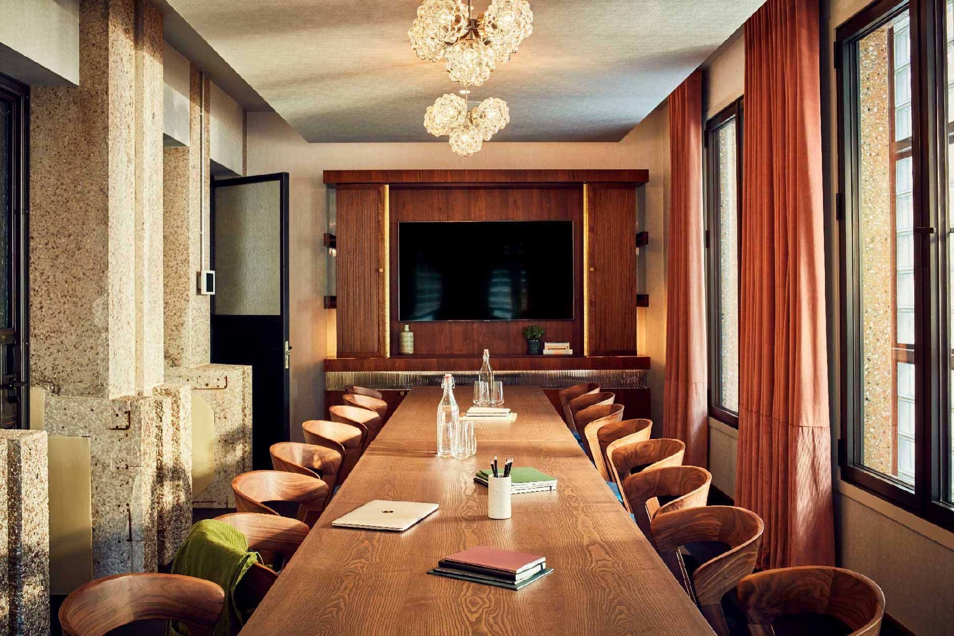 A stylish corporate meeting room with a long wooden table, ergonomic chairs, and a large presentation screen.
