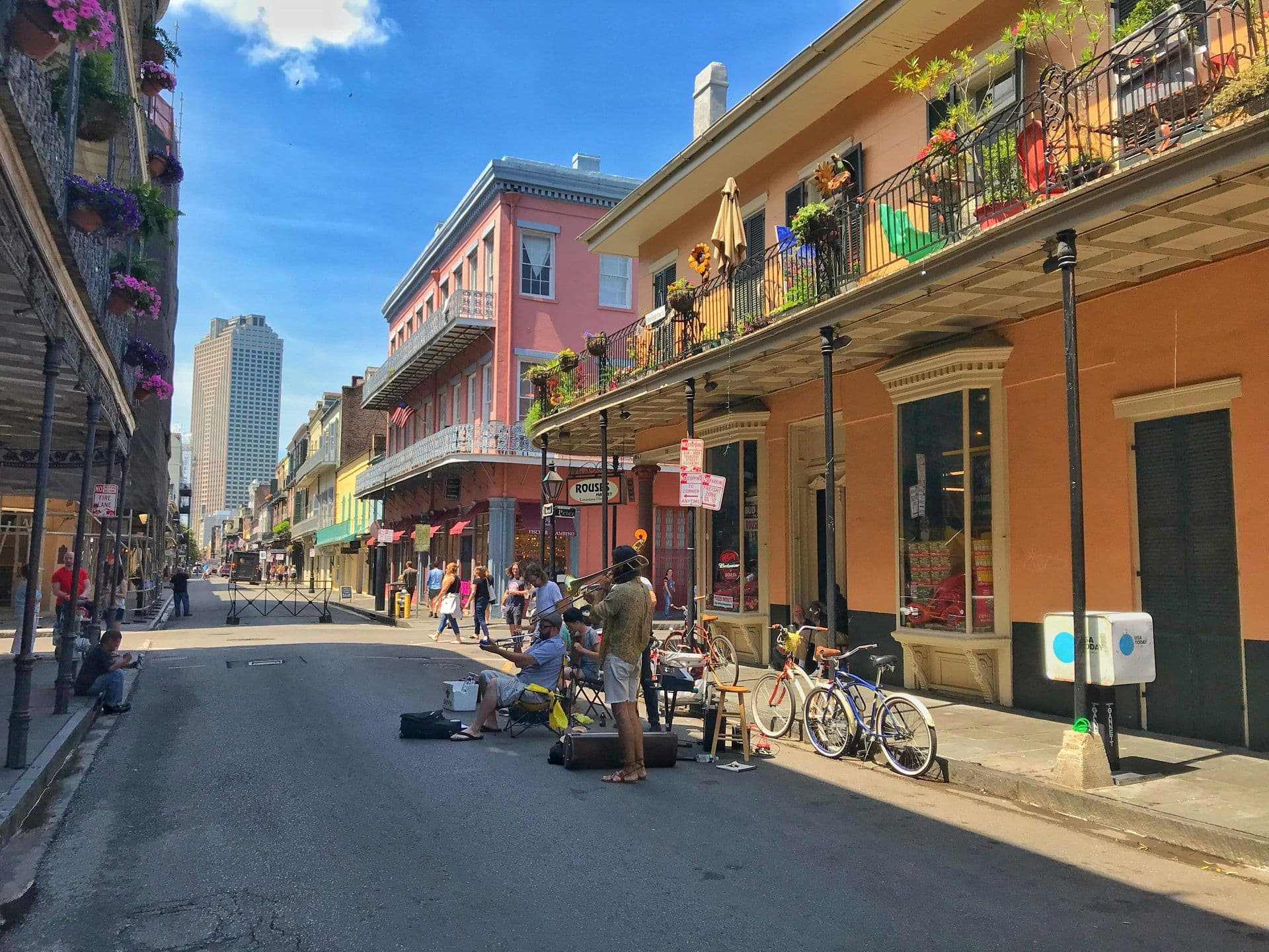 Historic street in New Orleans with colorful buildings, iron balconies, street musicians, and pedestrians.