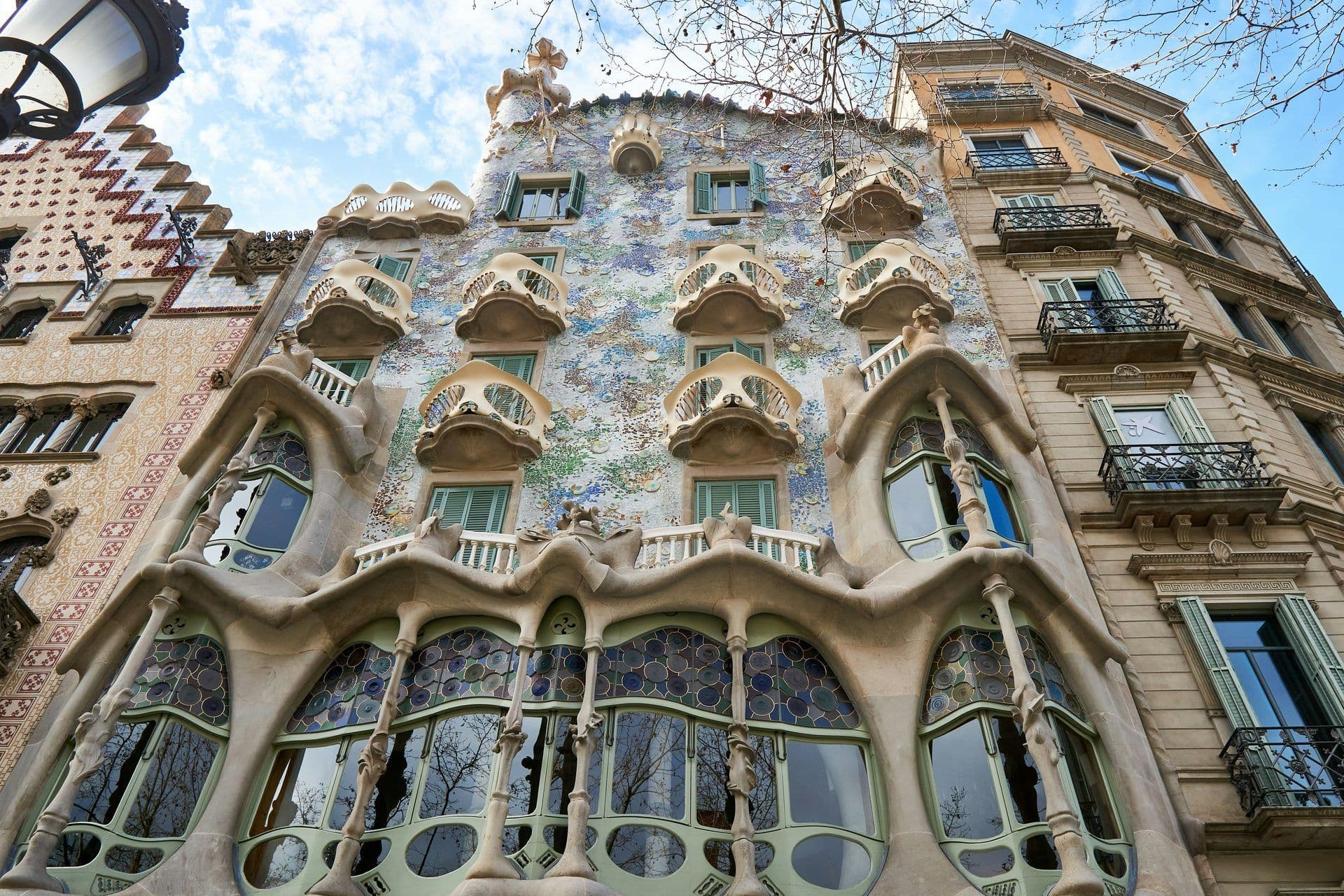 The unique, mosaic-covered facade of Casa Batlló, a historic venue in Barcelona, under a blue sky.