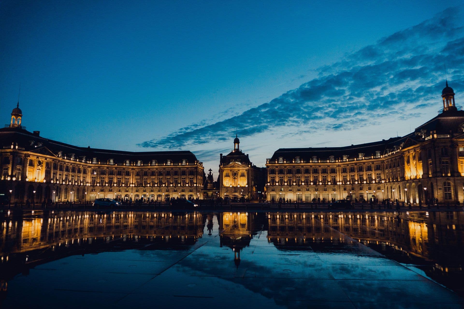 Grand historic venue in Bordeaux, France, illuminated and reflected in a water mirror at dusk.