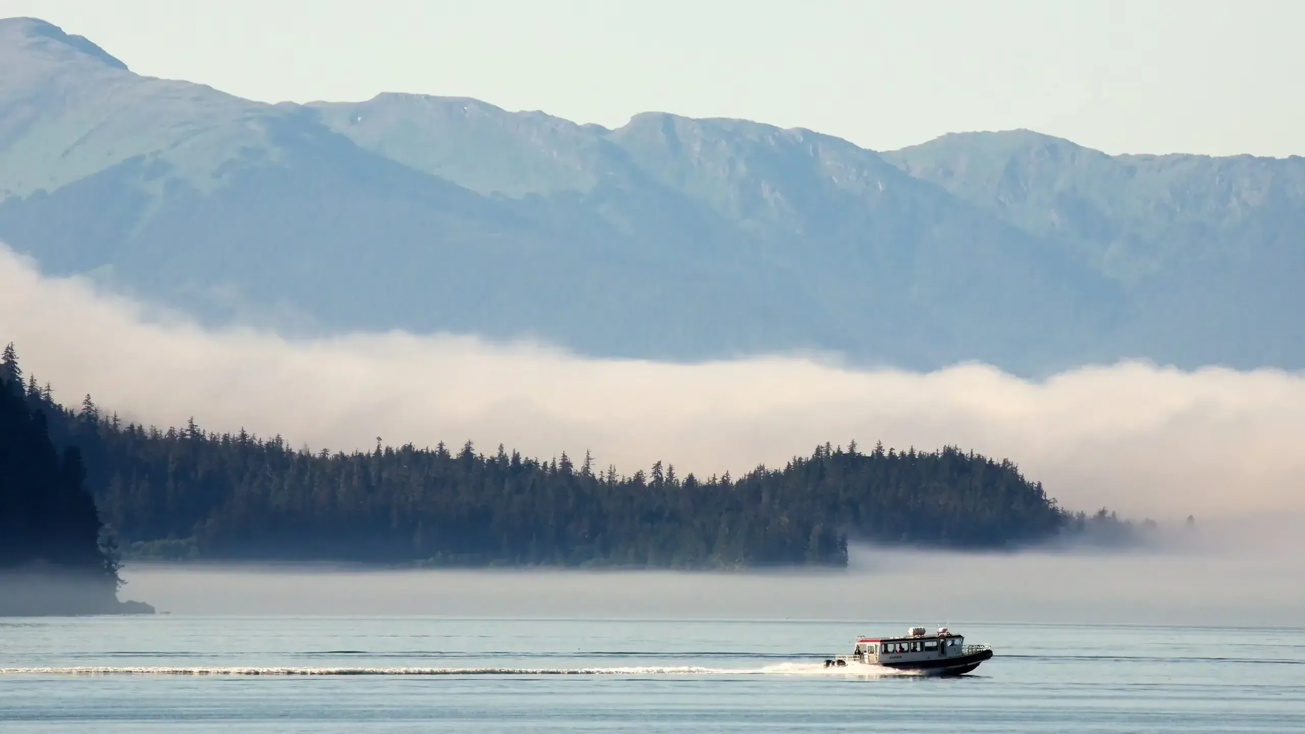 A motorboat cruises on misty waters with a forested island and mountains in Juneau, Alaska.