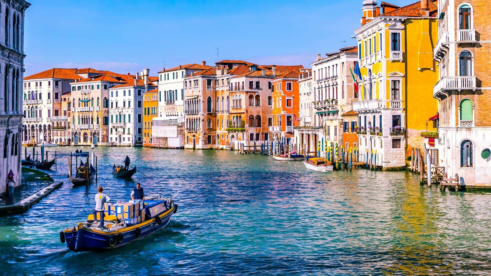 Colorful historic buildings line the Grand Canal in Venice, Italy, with gondolas and boats on the water.