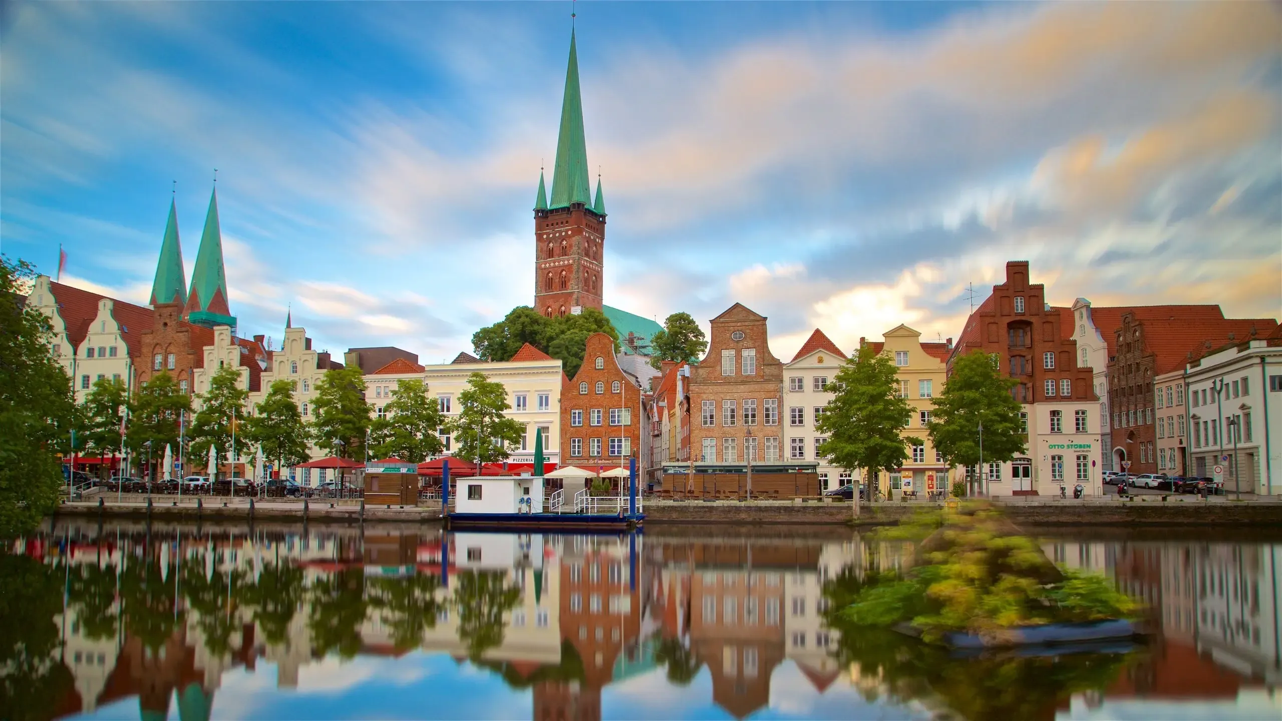 A scenic view of historic Lübeck, Germany, with gabled buildings and green spires reflected in the waterfront.