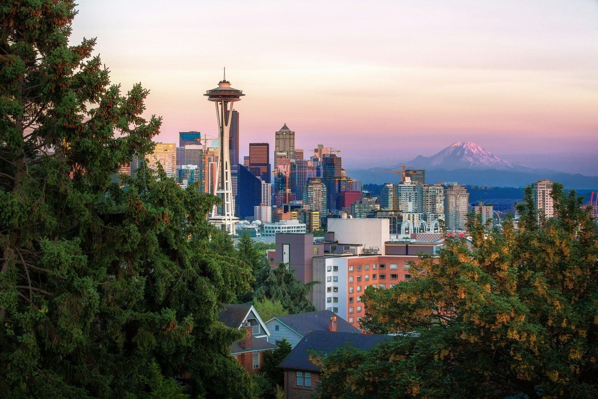 Seattle skyline at sunset featuring the Space Needle, downtown buildings, and Mount Rainier.