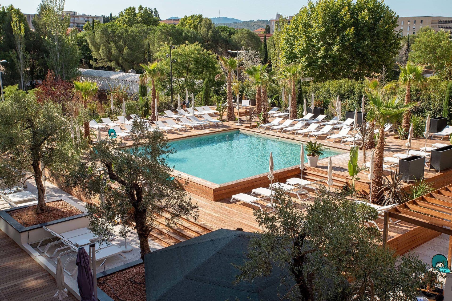 Sunny outdoor swimming pool with wooden deck, white loungers, and lush palm trees for corporate events.