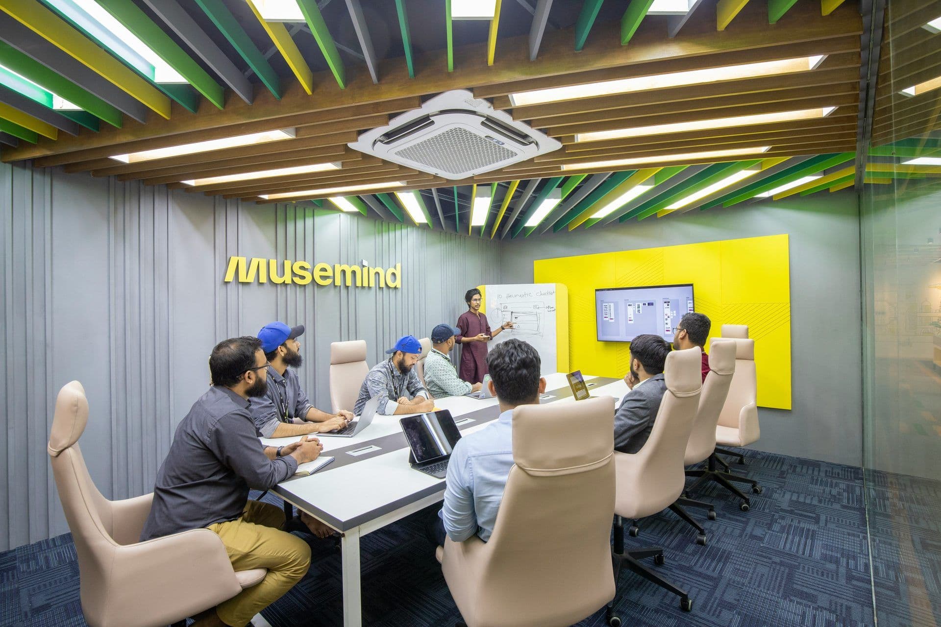 A team attends a workshop in a vibrant meeting room with a presenter, whiteboard, and digital display.