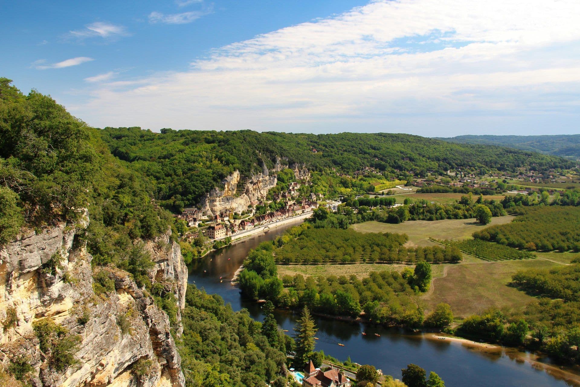 Panoramic view of a historic village built into cliffs along a river with kayaks