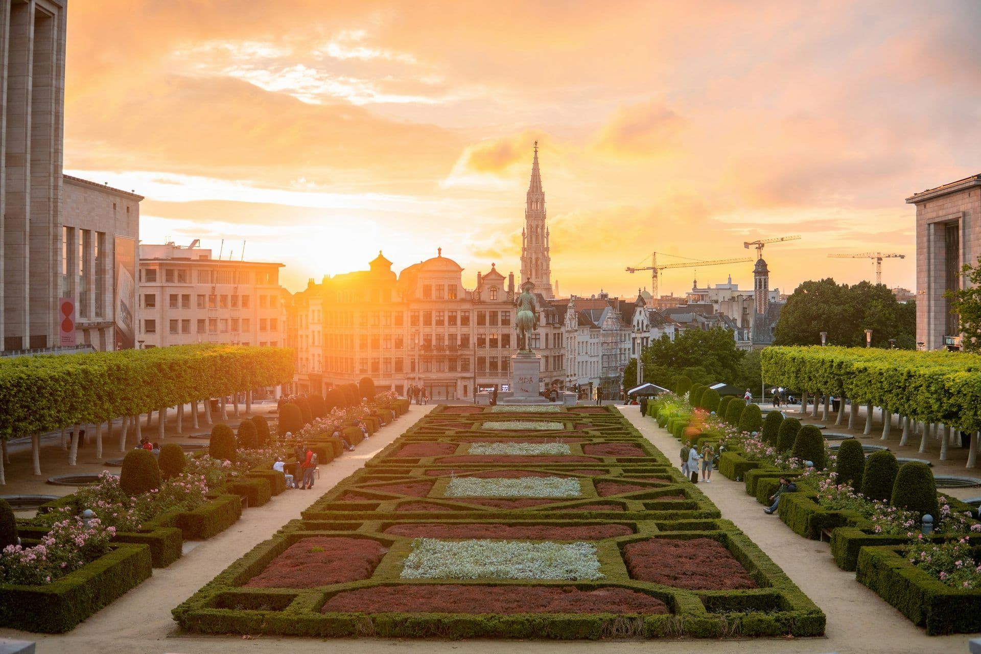 Mont des Arts formal gardens in Brussels at sunset, featuring historic buildings and a prominent spire.