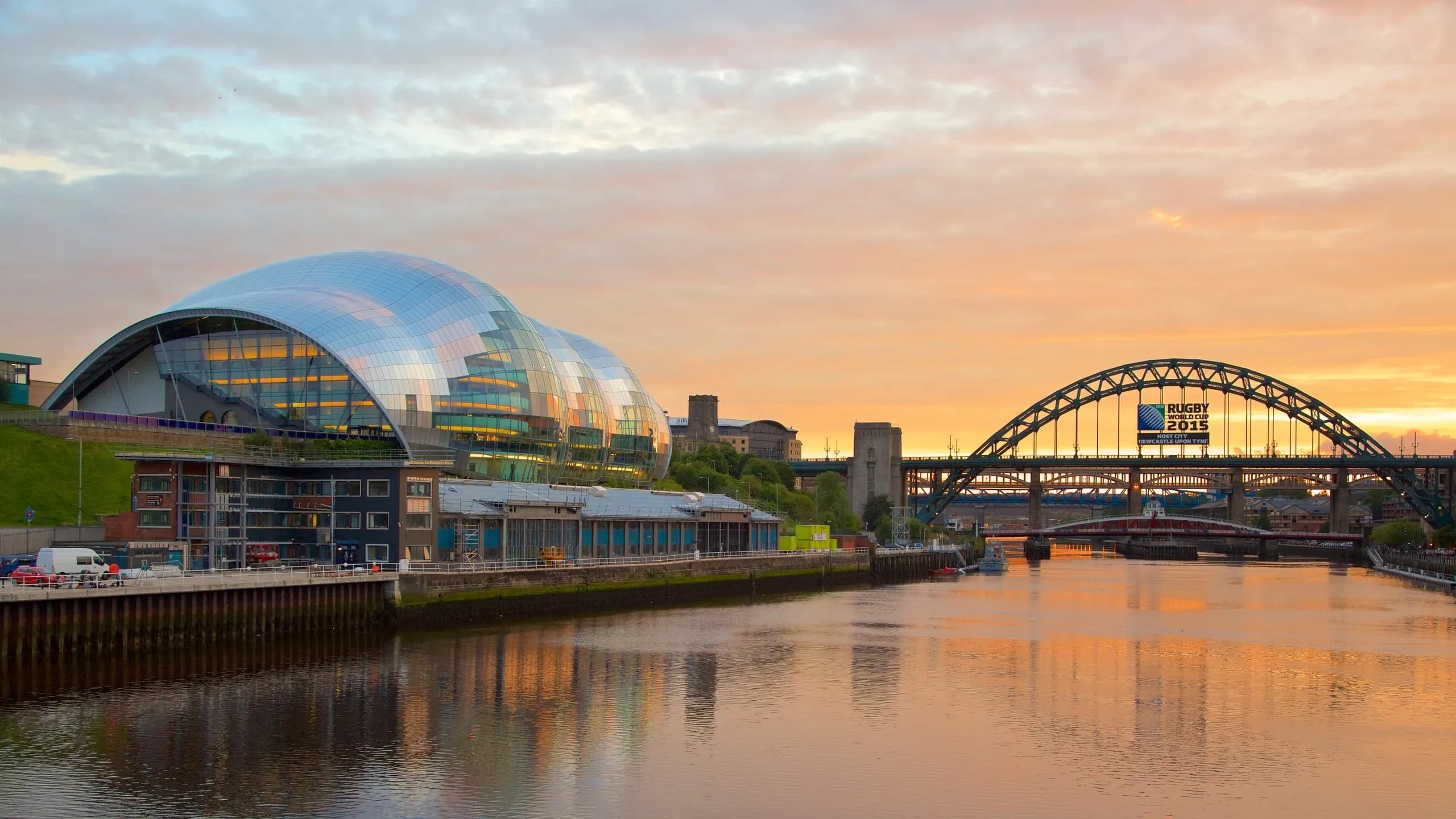 Modern waterfront event venue, Sage Gateshead, and Tyne Bridge at sunset in Newcastle upon Tyne.