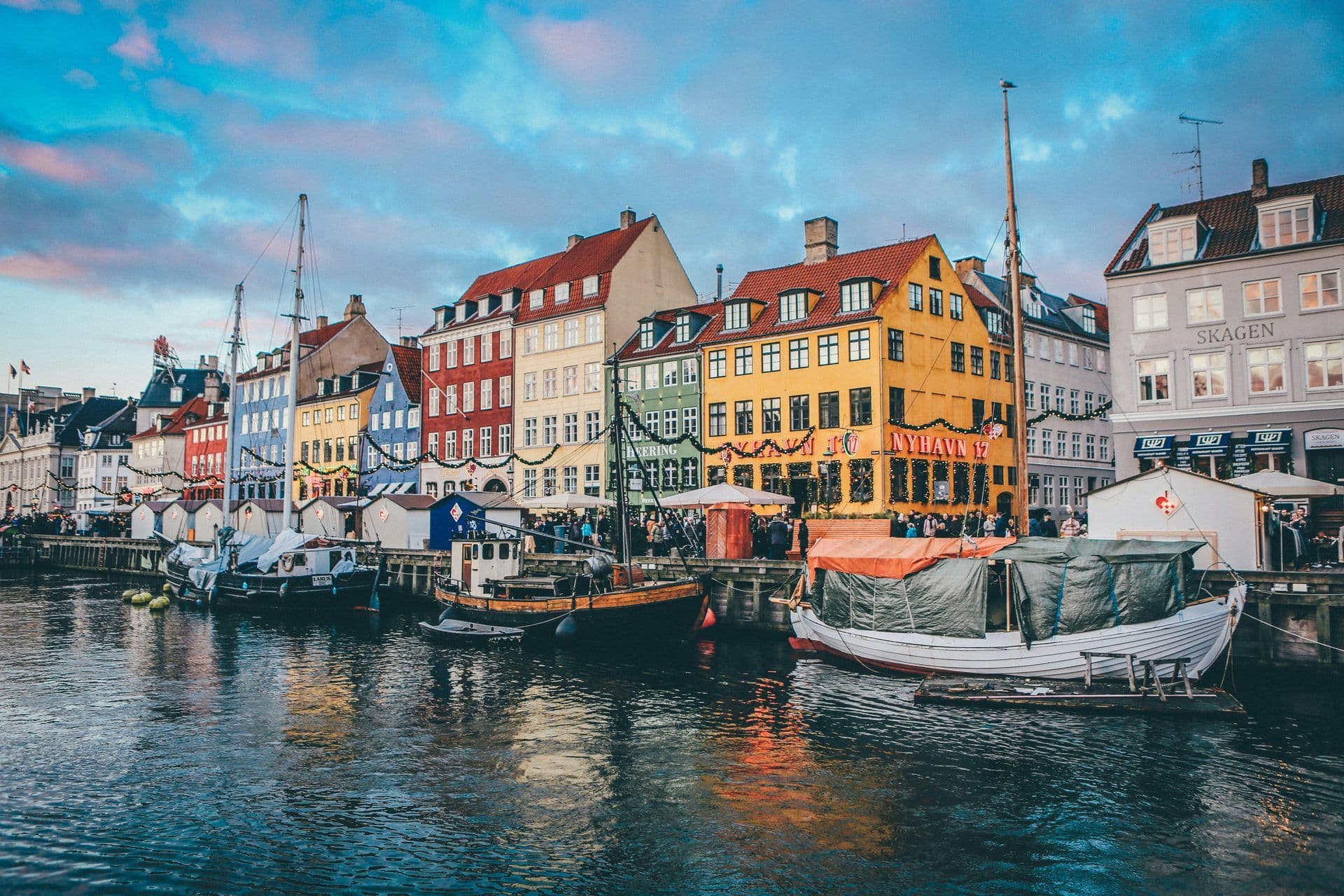 Colorful historic buildings and boats line the Nyhavn canal in Copenhagen, Denmark, with festive lights.