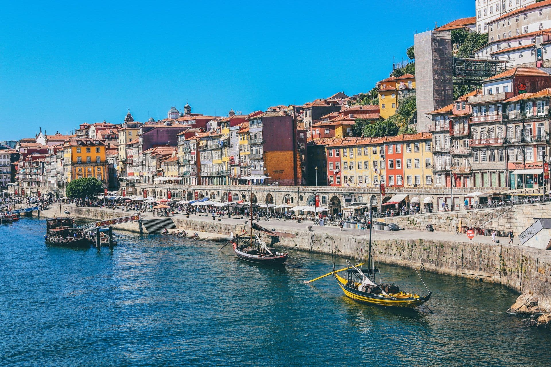 Vibrant Porto, Portugal waterfront with colorful historic buildings, Rabelo boats, and outdoor dining.