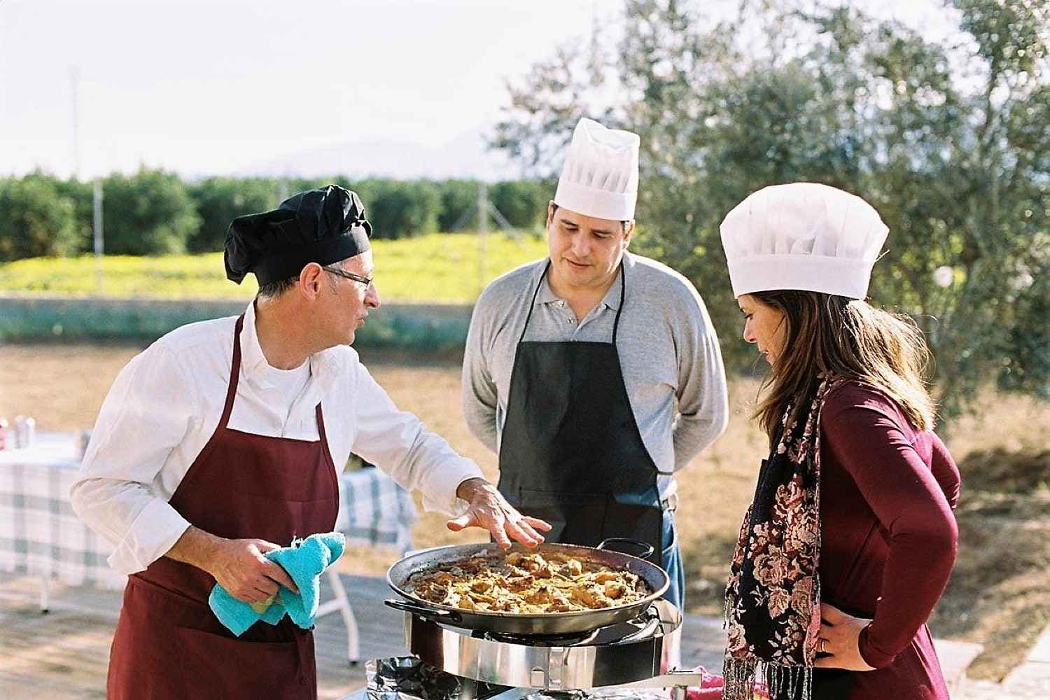 Three people in chef hats cooking paella outdoors during a corporate team building activity.