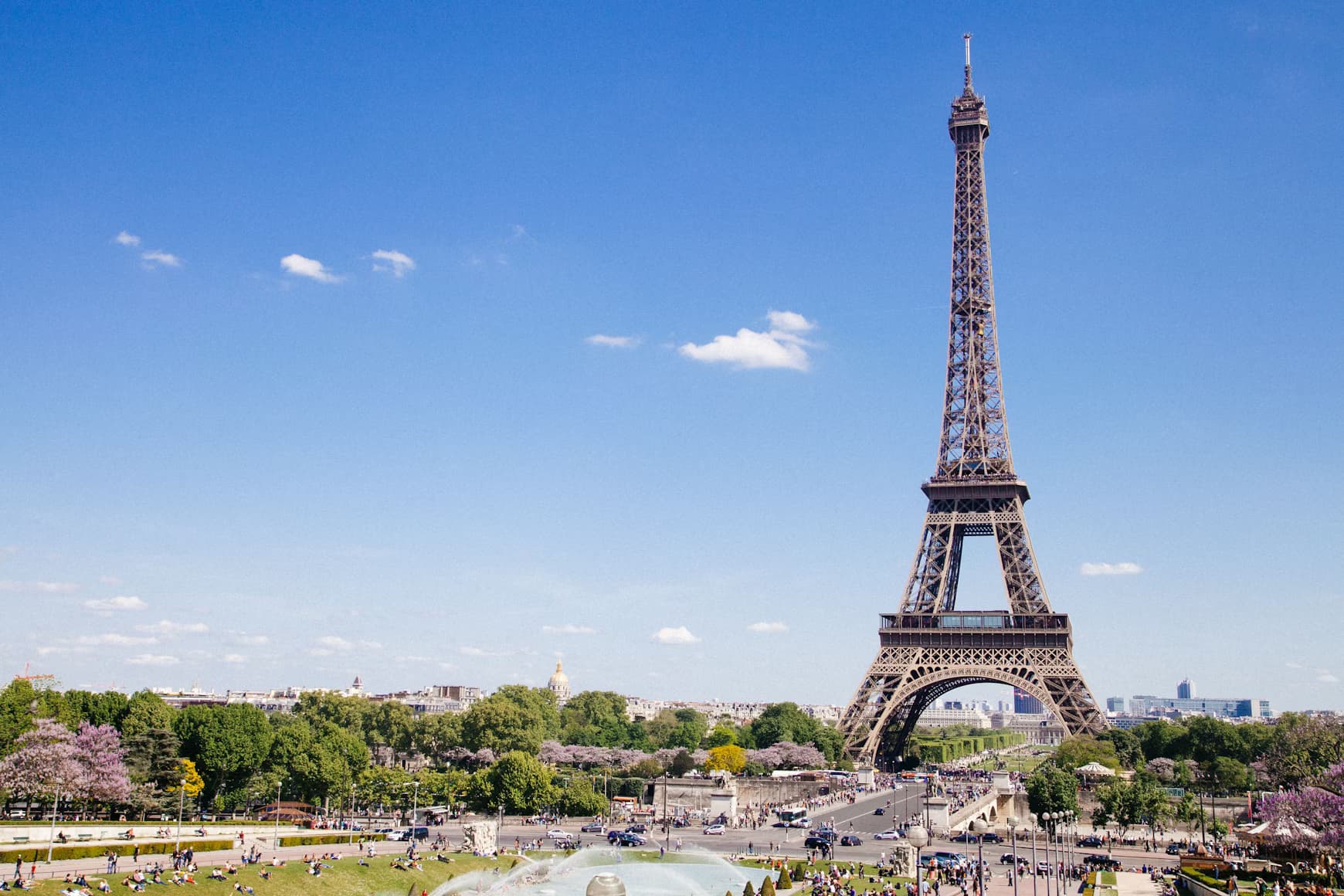 The iconic Eiffel Tower in Paris, France, with a bustling park and city view under a clear blue sky.