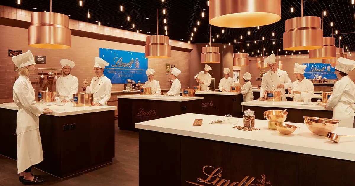 Attendees in chef hats enjoy a chocolate cooking class team building activity at a Lindt workshop venue.