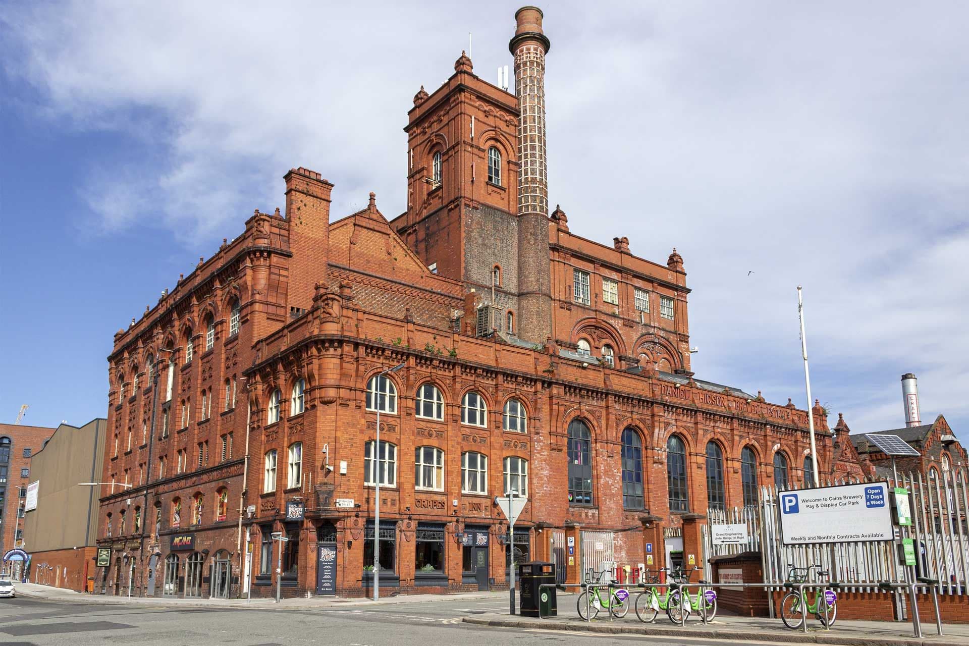 Exterior of a grand red brick historic brewery building with a tall chimney in Liverpool, UK.