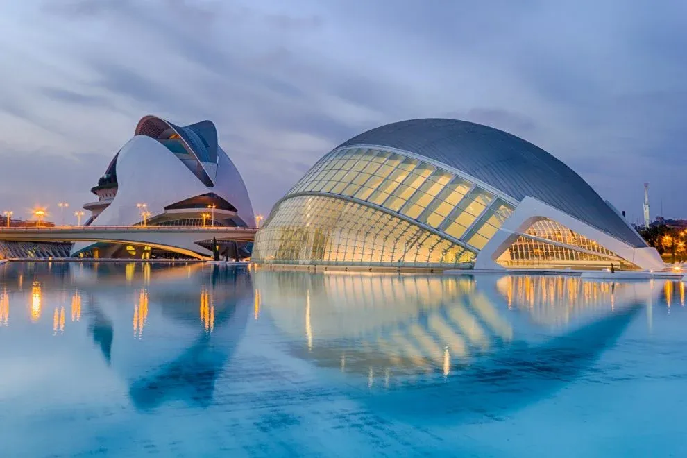 Modern architectural corporate event venues in Valencia, Spain, reflected in a tranquil water pool at dusk.
