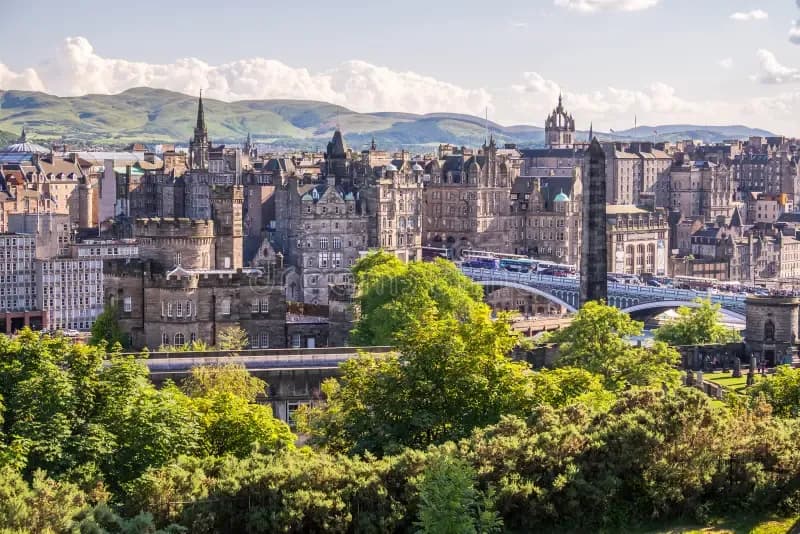 Panoramic view of historic Edinburgh, Scotland, with old buildings, a bridge, and green hills.