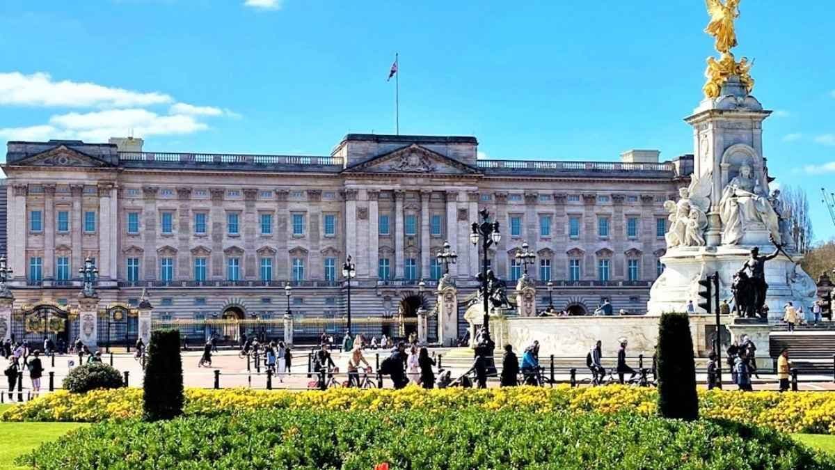 Historic Buckingham Palace and Victoria Memorial in London, surrounded by green lawns and yellow flowers.