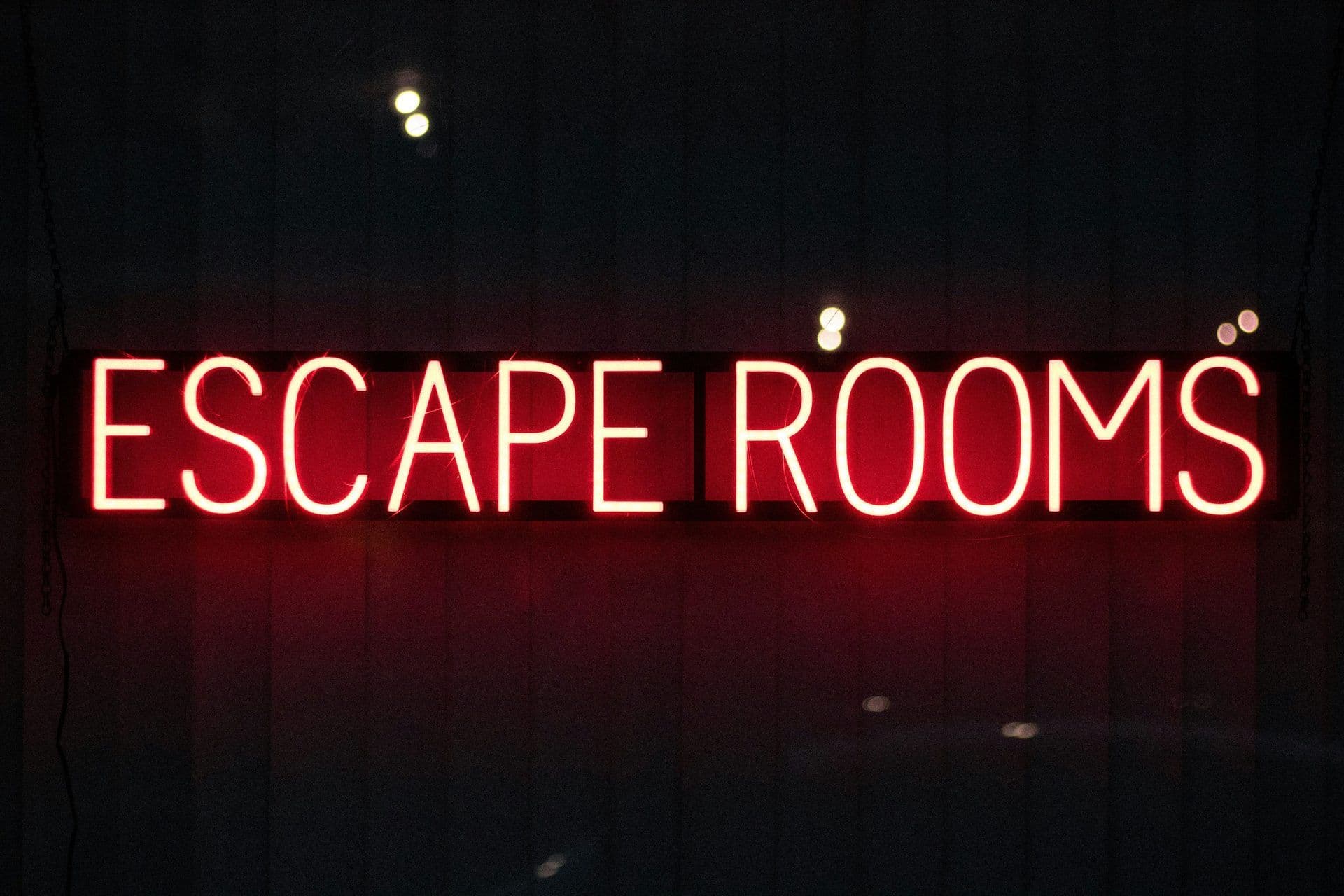 A bright red neon sign illuminates the words "ESCAPE ROOMS" against a dark background.