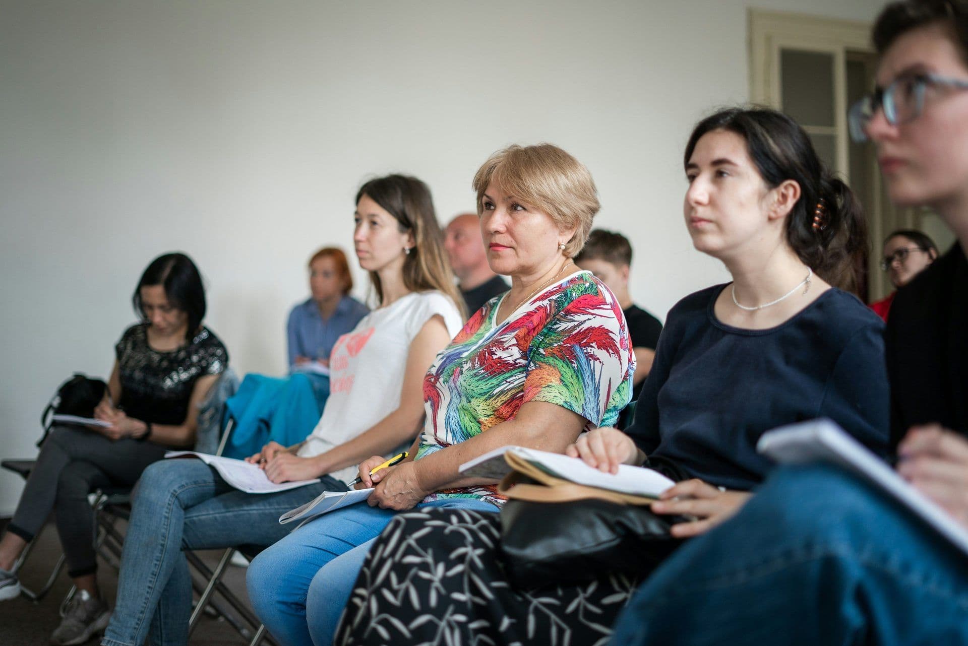 Diverse group of professionals attending a corporate seminar, taking notes in a modern event space.