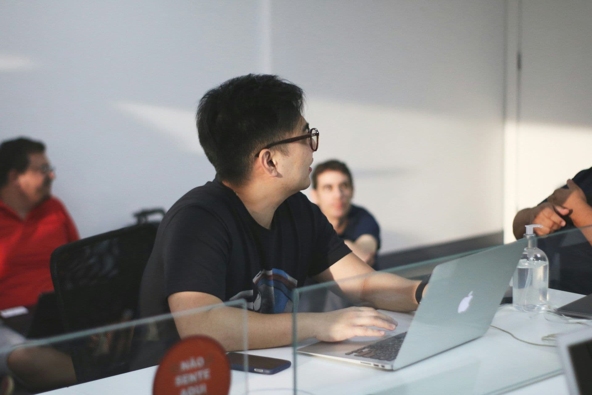 Man with laptop at a corporate event in a modern meeting room with a social distancing sign.
