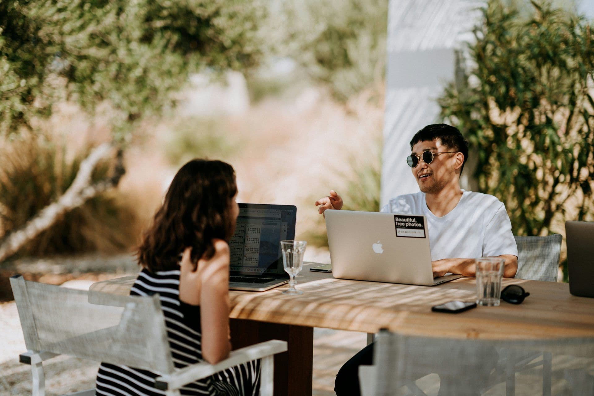 Two people work on laptops at an outdoor wooden table, ideal for a team offsite or corporate retreat.