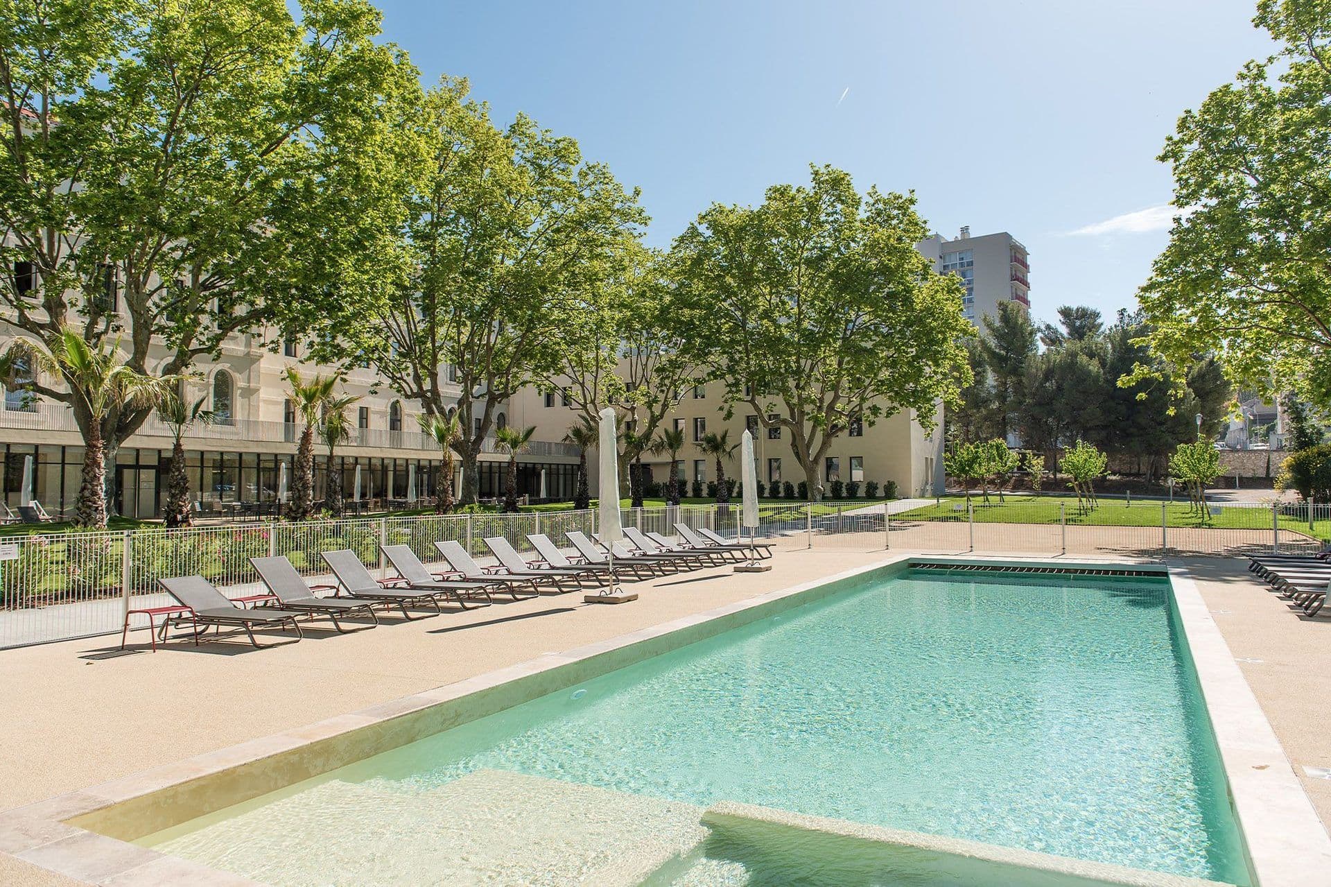 Large outdoor swimming pool with sun loungers at a corporate event venue, surrounded by trees.