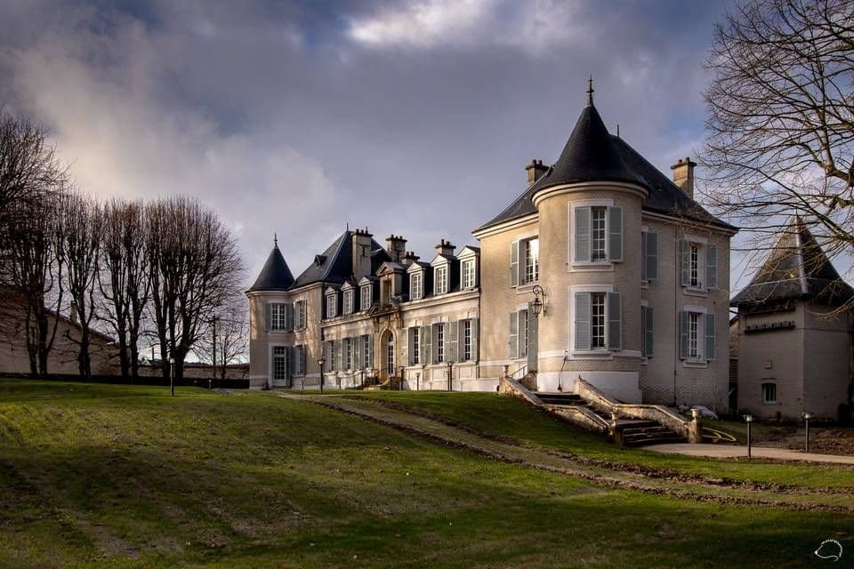 An elegant historic chateau, a corporate event venue with turrets and light blue shutters, on a green lawn.