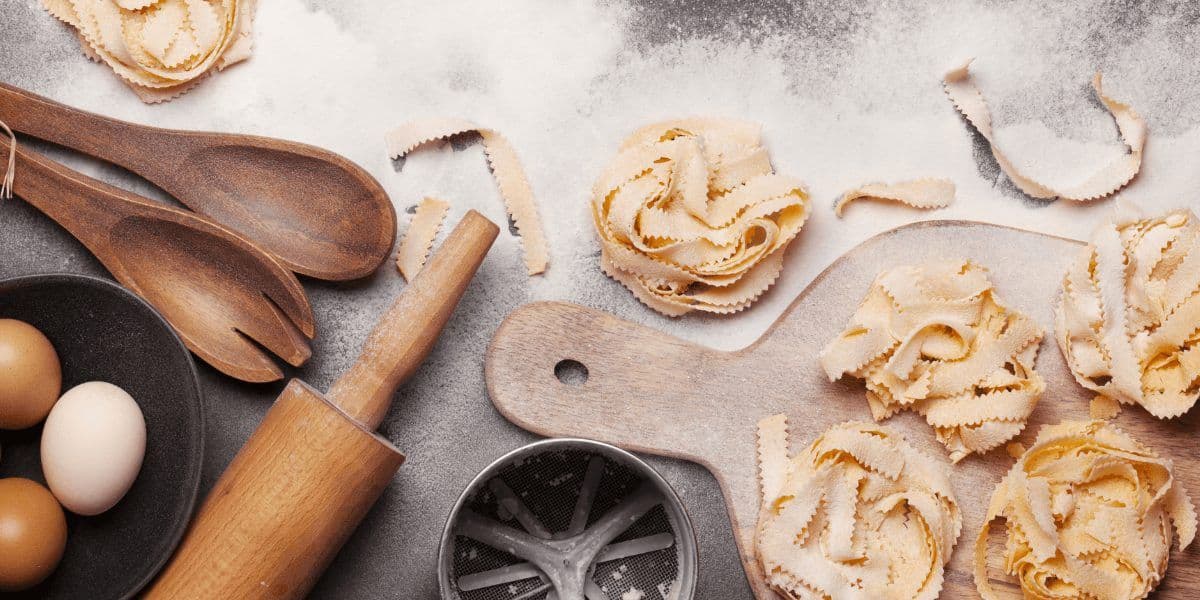 Ingredients and tools for a cooking class, including fresh pasta, eggs, flour, rolling pin, and wooden spoons.