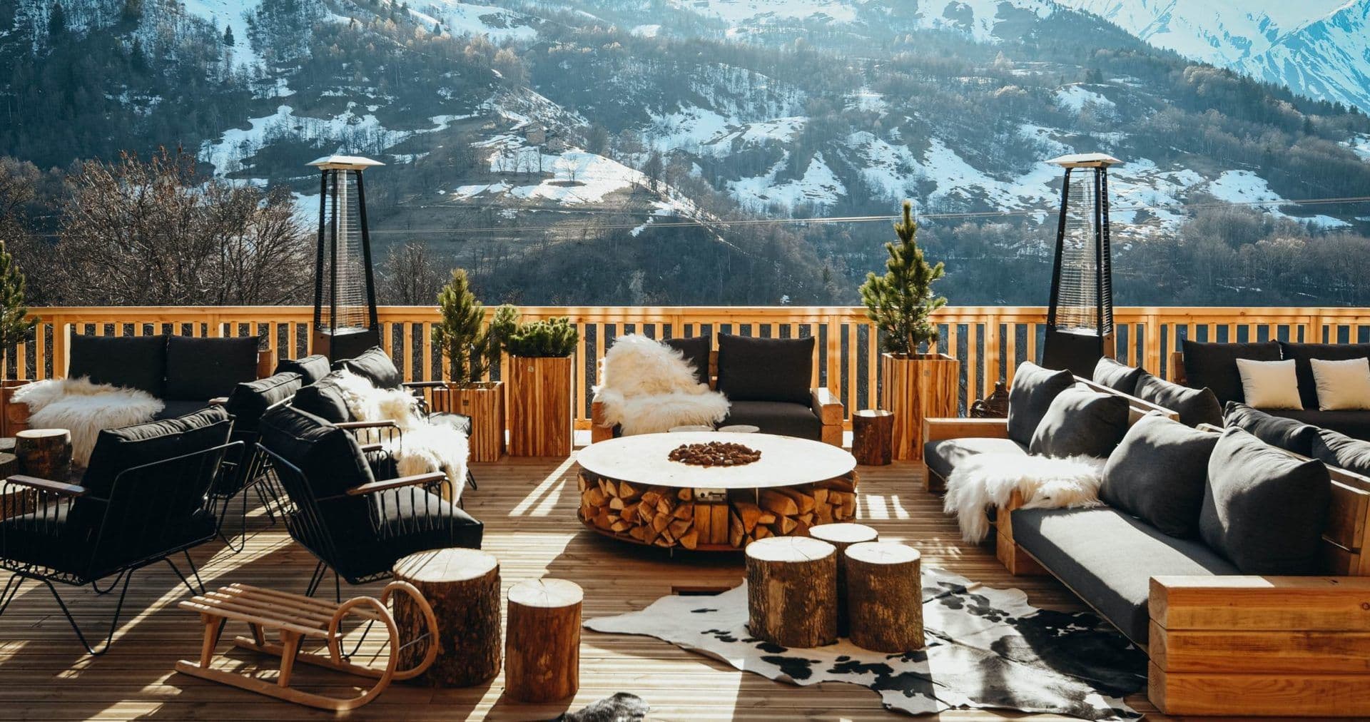 Spacious outdoor terrace with a fire pit and cozy seating, offering stunning views of the snowy French Alps.