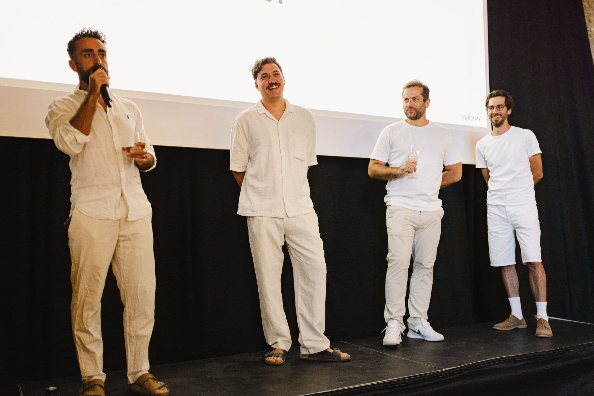 Four men on stage presenting at a corporate event, one speaking into a microphone