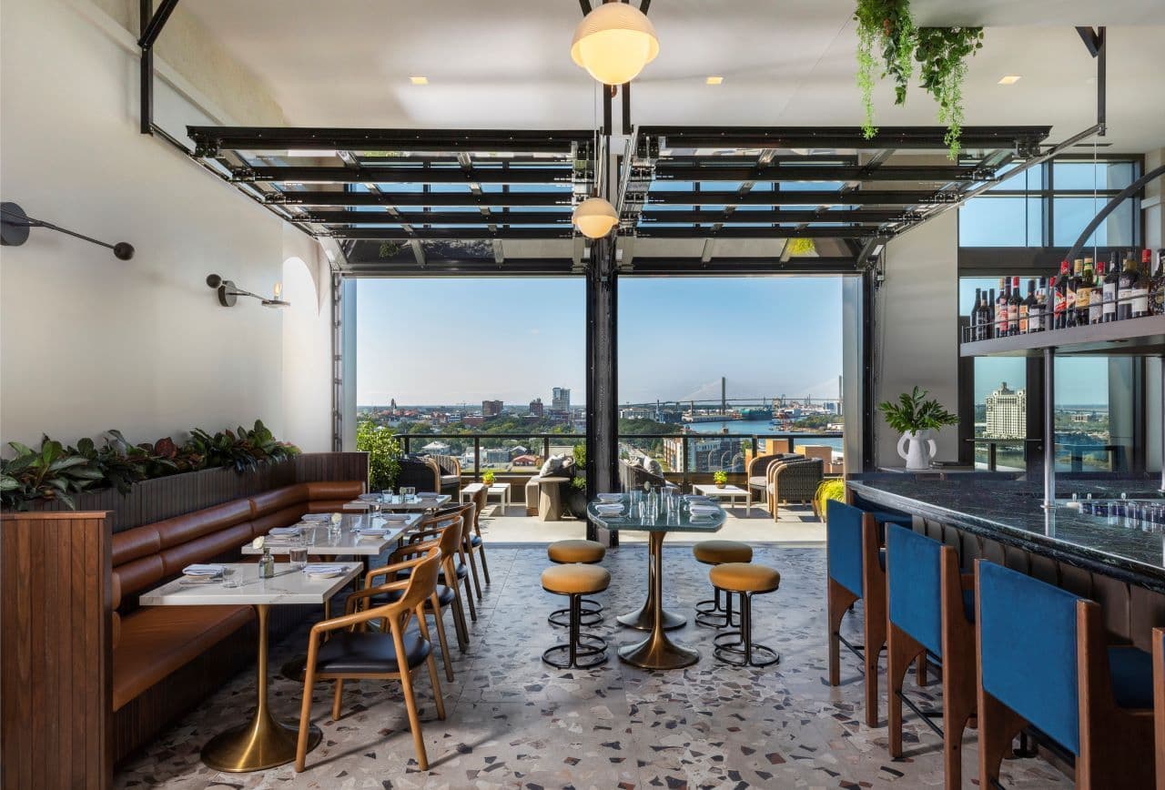 A modern rooftop event space in Savannah with indoor-outdoor seating, a bar, and a city skyline view.