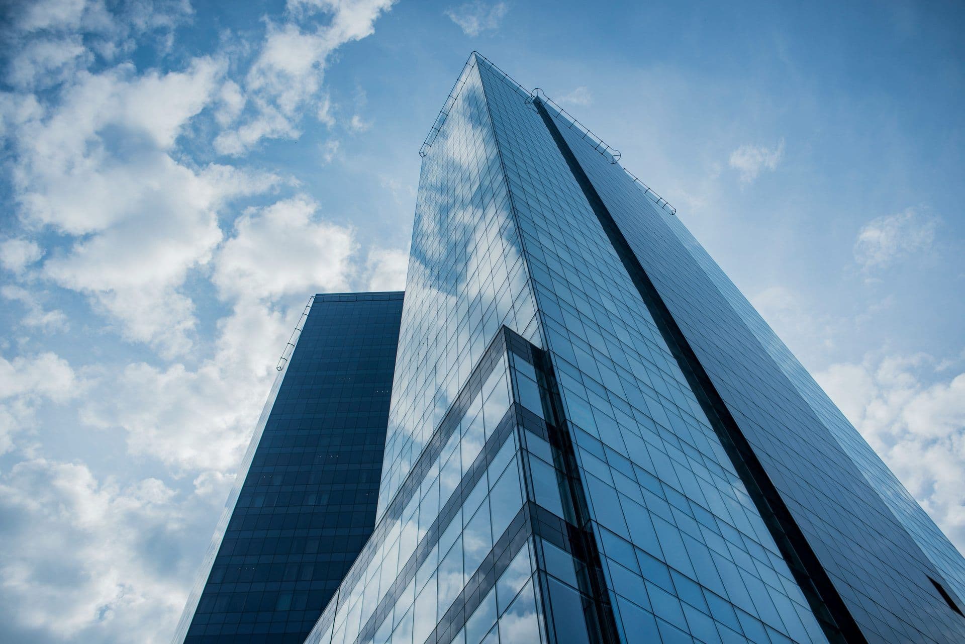 Two modern glass skyscrapers reflect a cloudy blue sky, suitable for a corporate event venue.