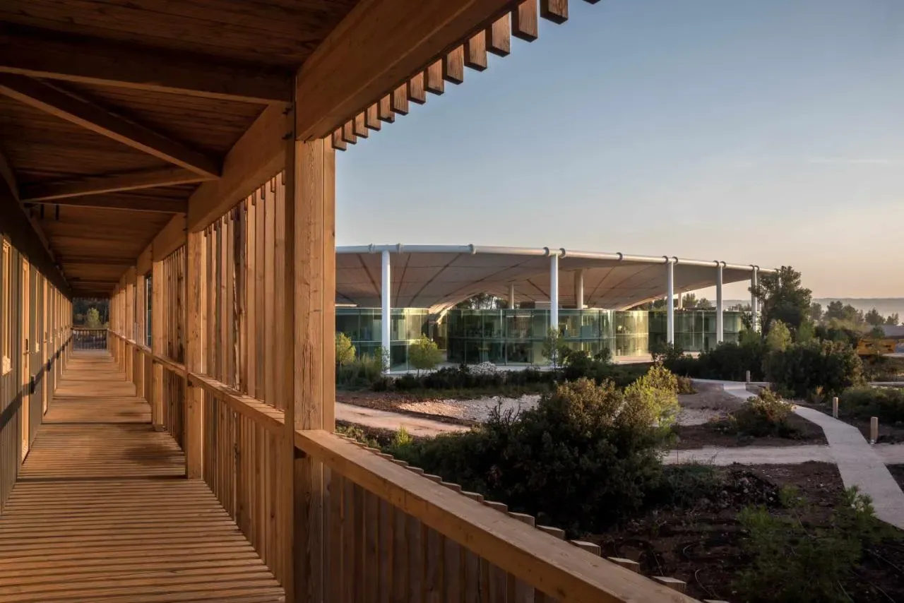 Long wooden walkway overlooking a modern corporate event venue with a large canopy roof and glass walls