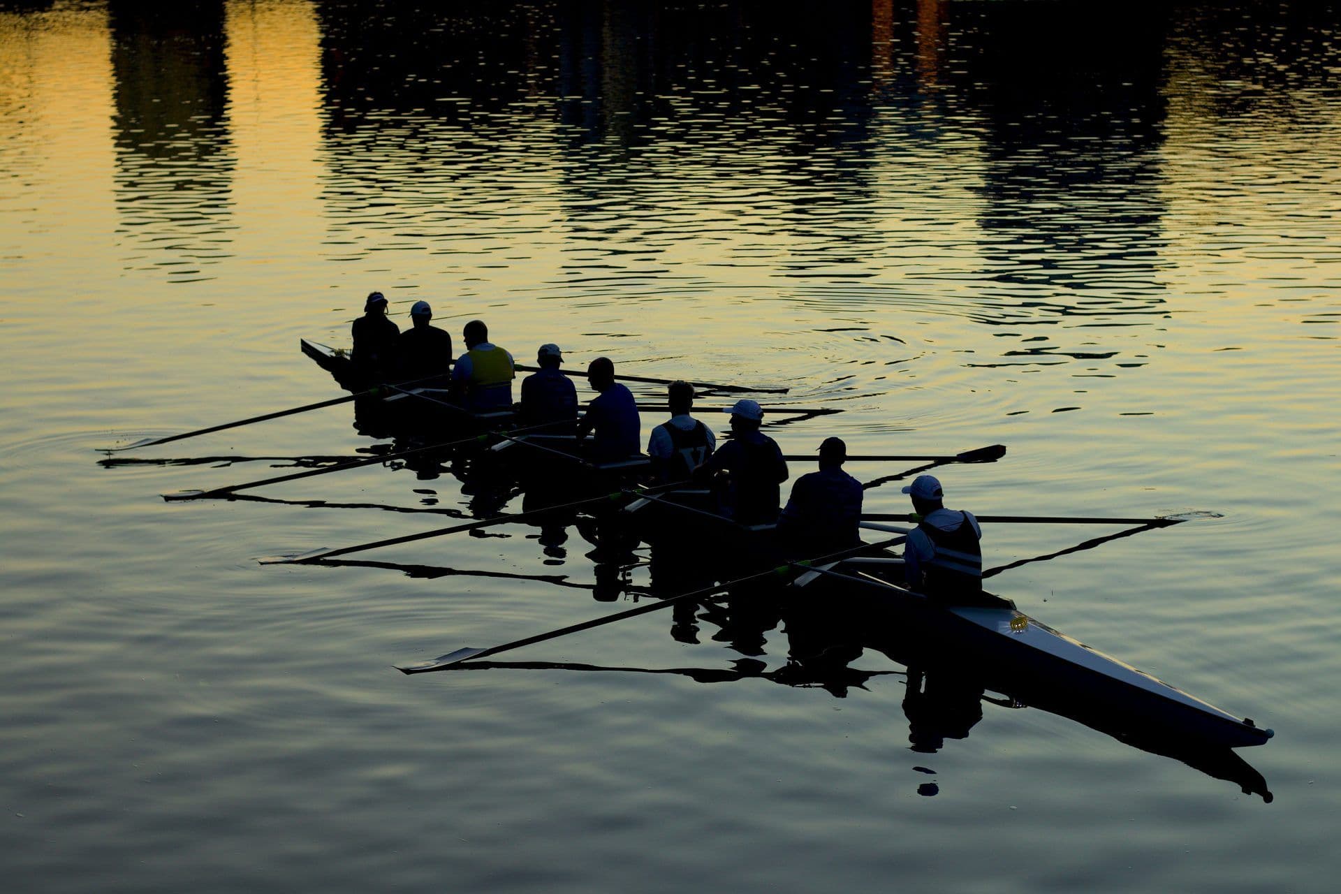 Eight people in a rowing boat on calm water at sunset, perfect for a team building activity.